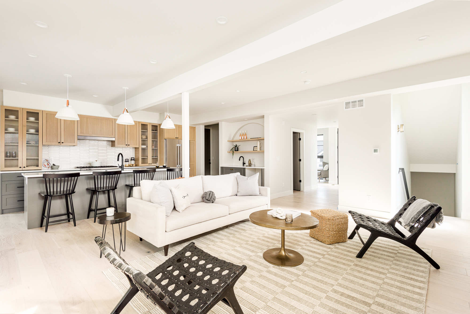 Open living room with a white sofa, woven chairs and a brass coffee table, with the kitchen island behind