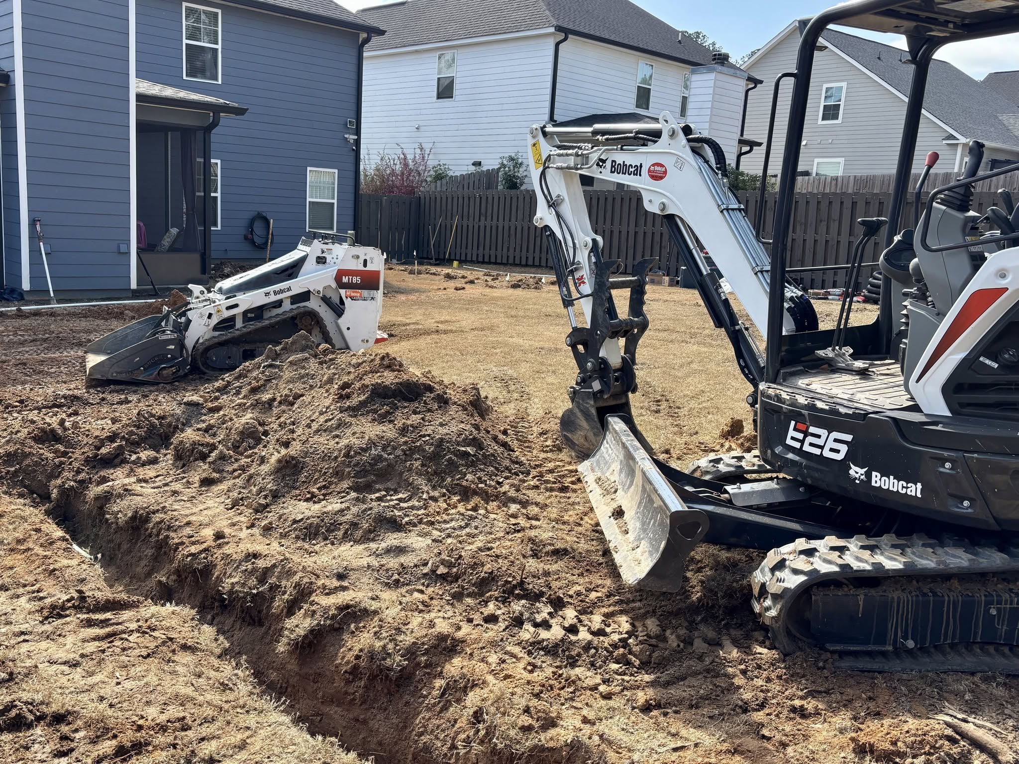 Excavator and skid steer trenching a backyard for drainage