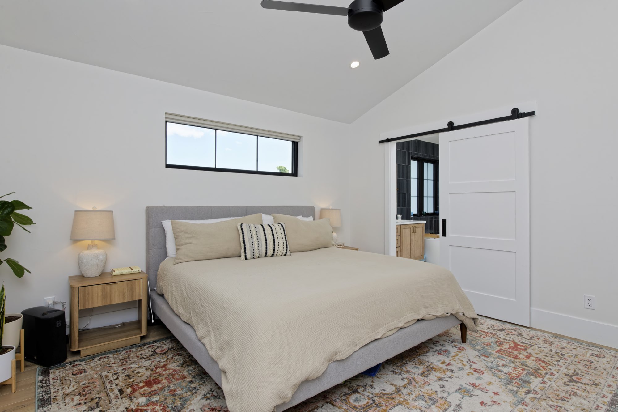 Primary bedroom with a vaulted ceiling, ceiling fan, wood floors and a sliding white barn door to the bath