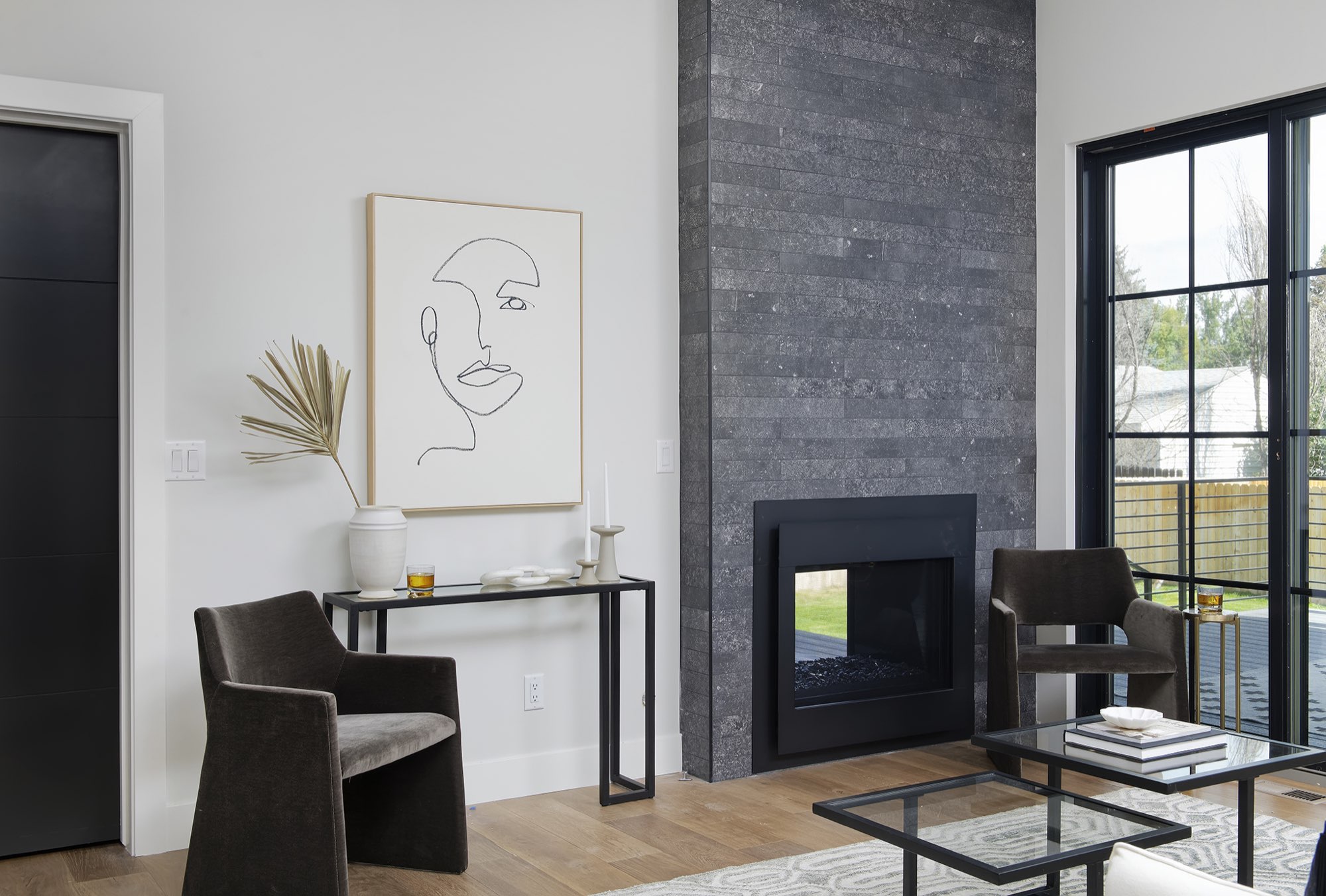 Dark stone fireplace wall beside a black interior door and black-framed glass doors to the deck