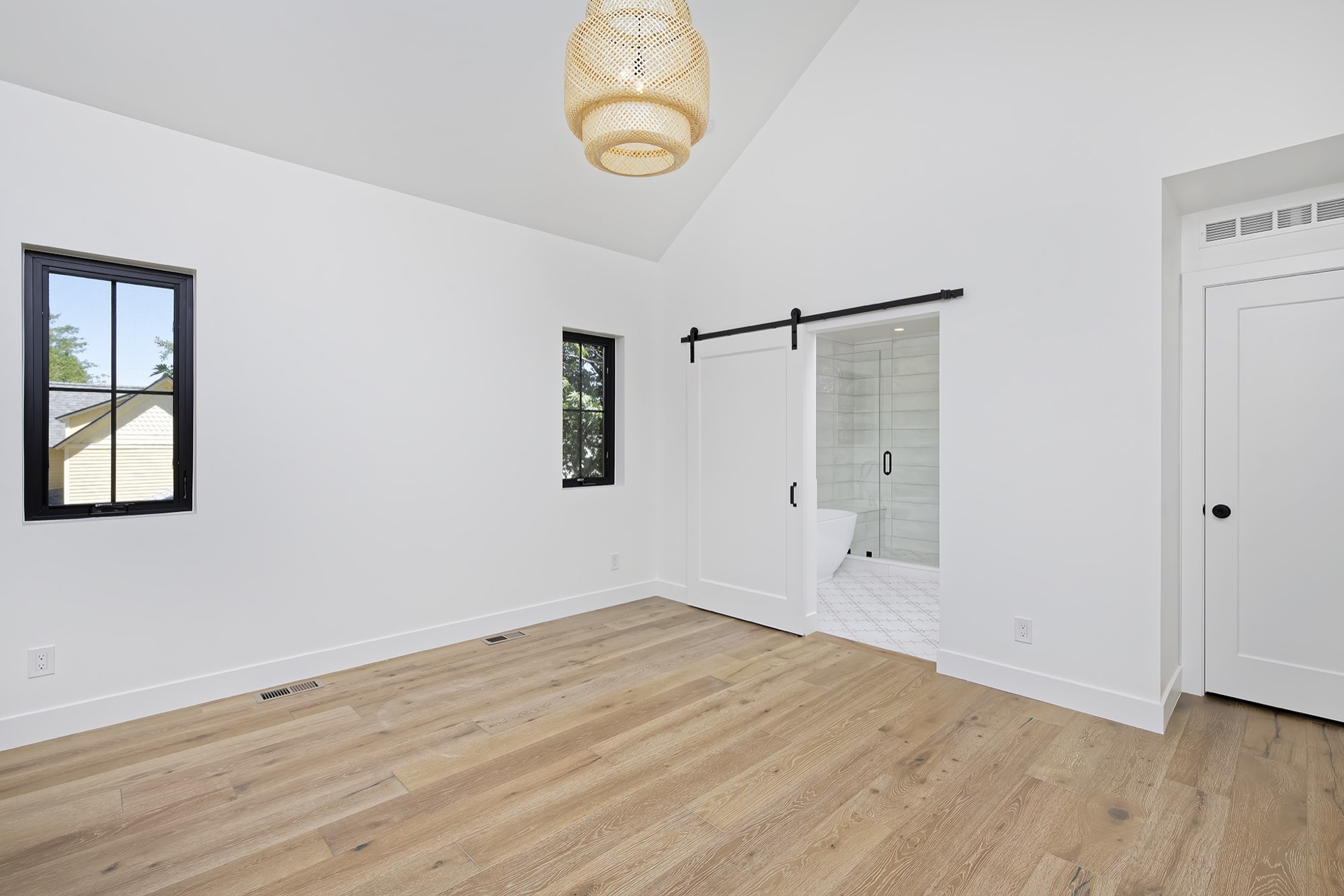 Bedroom corner with black-framed windows, a woven pendant and a view into the bath