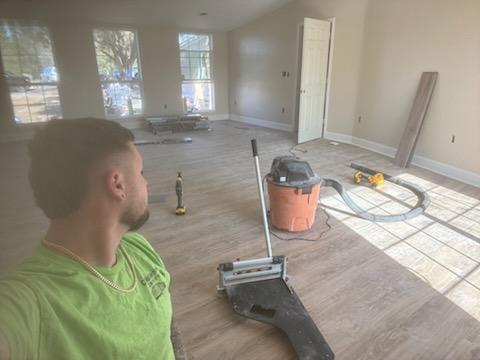 Luxury vinyl plank going down in a mobile home living room with a tapping block and shop vacuum on the floor