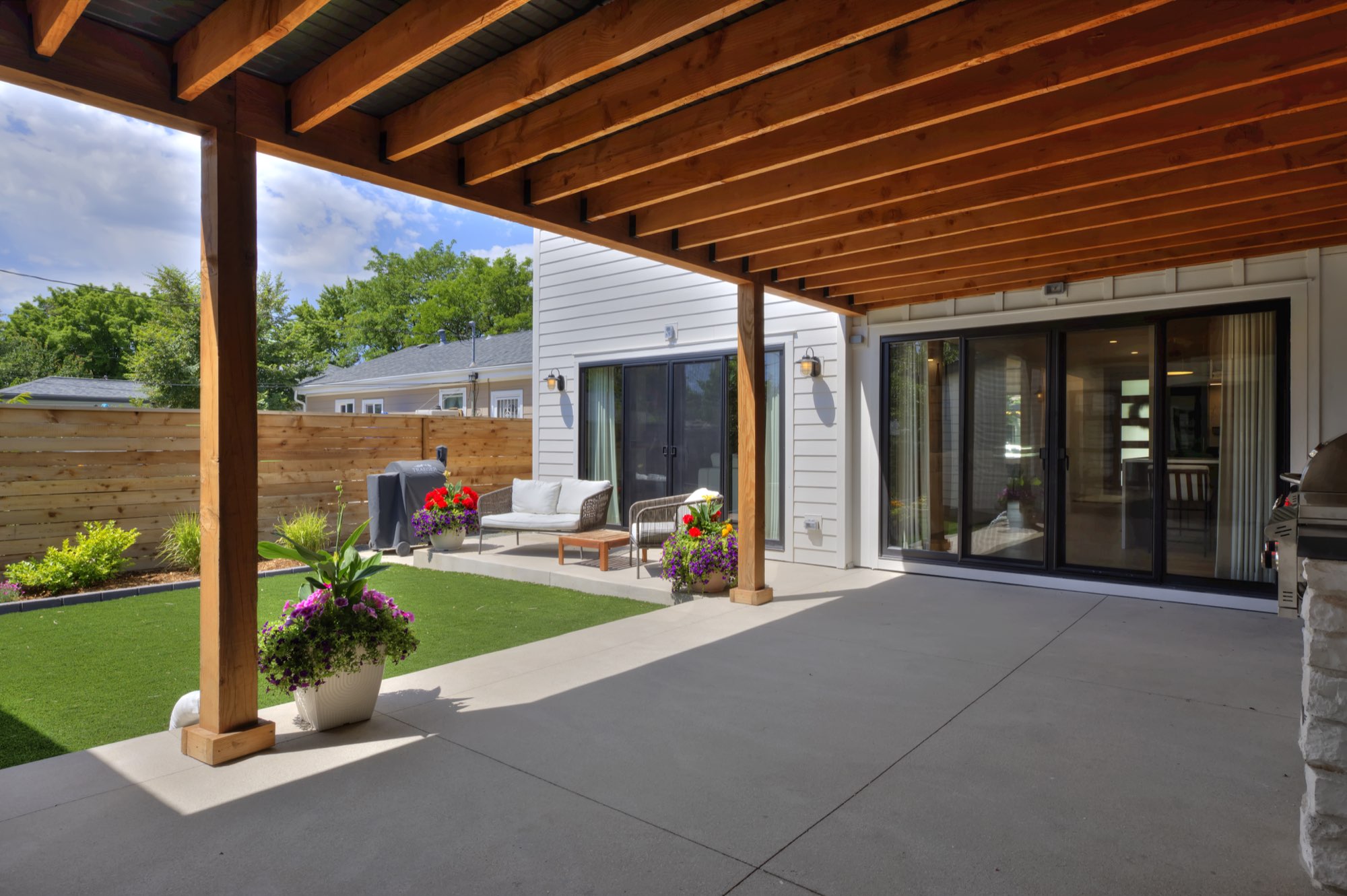Covered concrete patio looking toward the back sliding doors and a seating area on the lawn