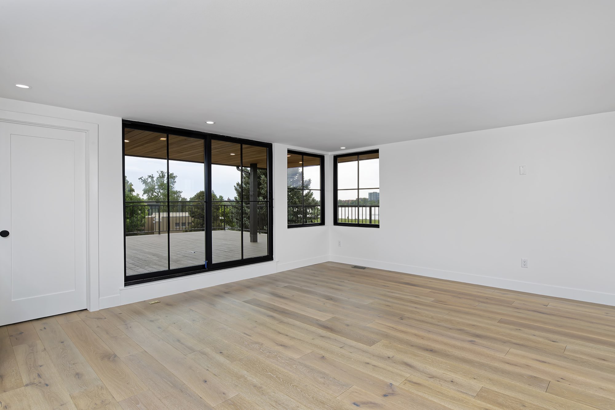 Upper lounge with wide-plank floors and black-framed sliding doors opening to the deck