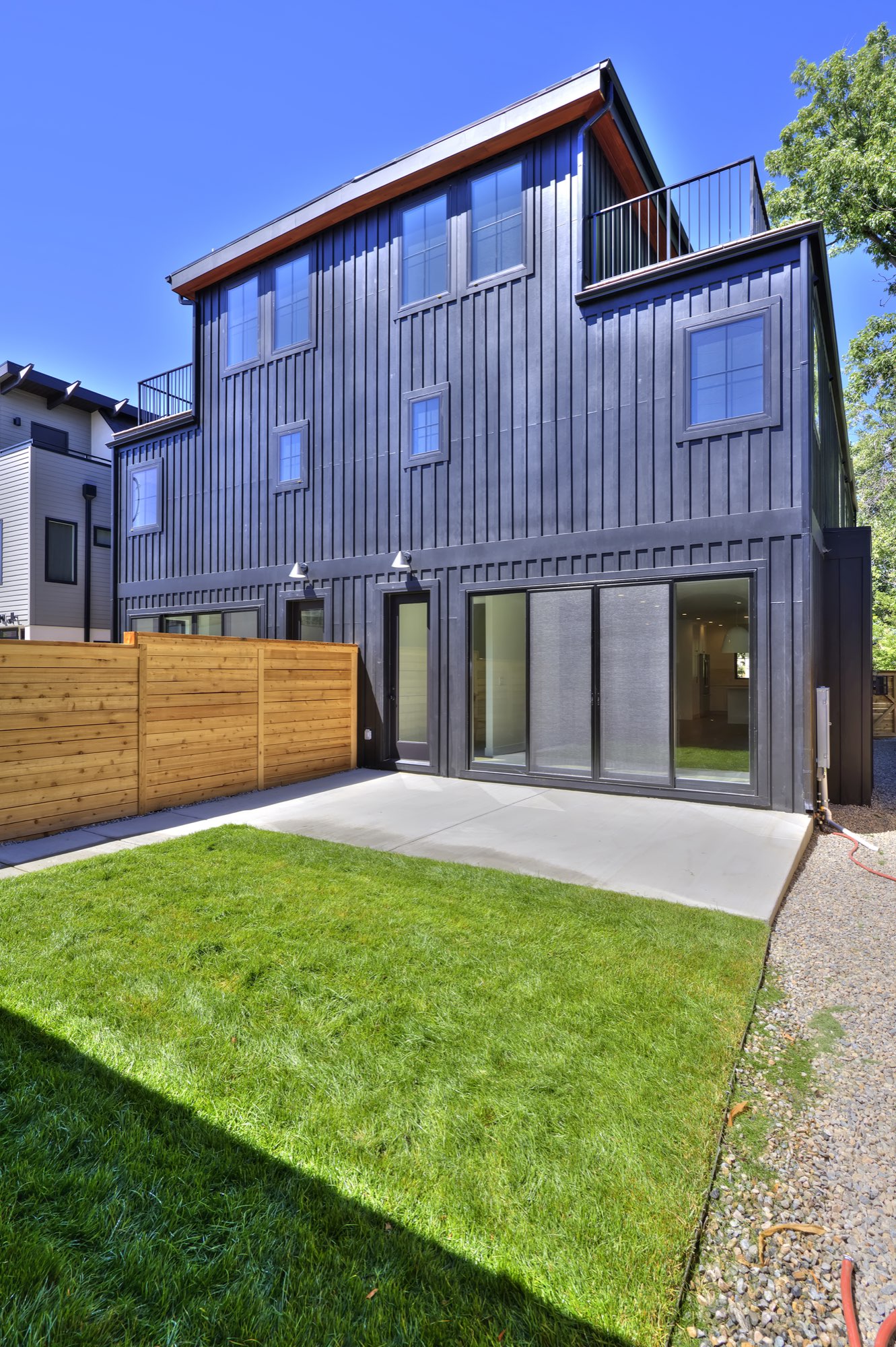 Rear of the Nordic farmhouse duplex with black vertical siding, a roof deck railing and sliding doors to the patio