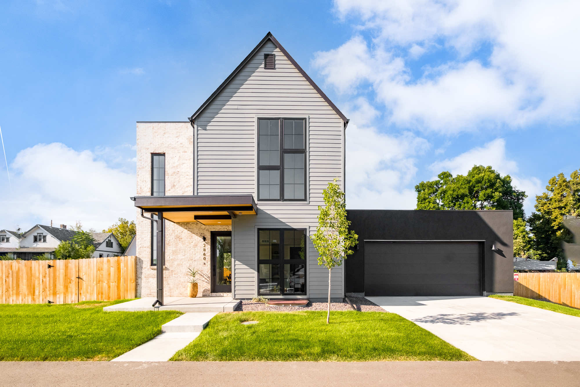 Front of the new custom home in Wheat Ridge with a gray gable, pale brick entry, dark shingle roof and a dark two-car garage