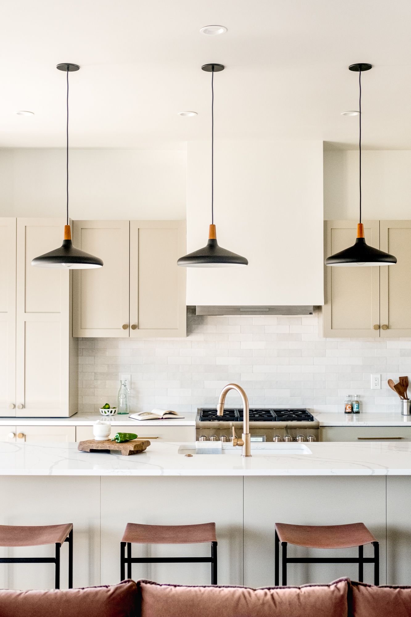Kitchen with a large white island, leather saddle stools, three black pendants and cabinets to the ceiling