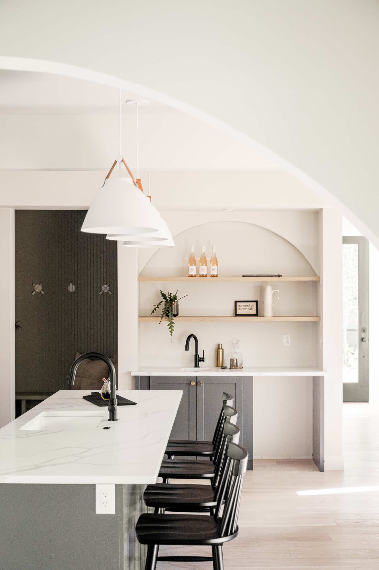 White pendants over the kitchen island, looking through the arch to the wet bar and mudroom