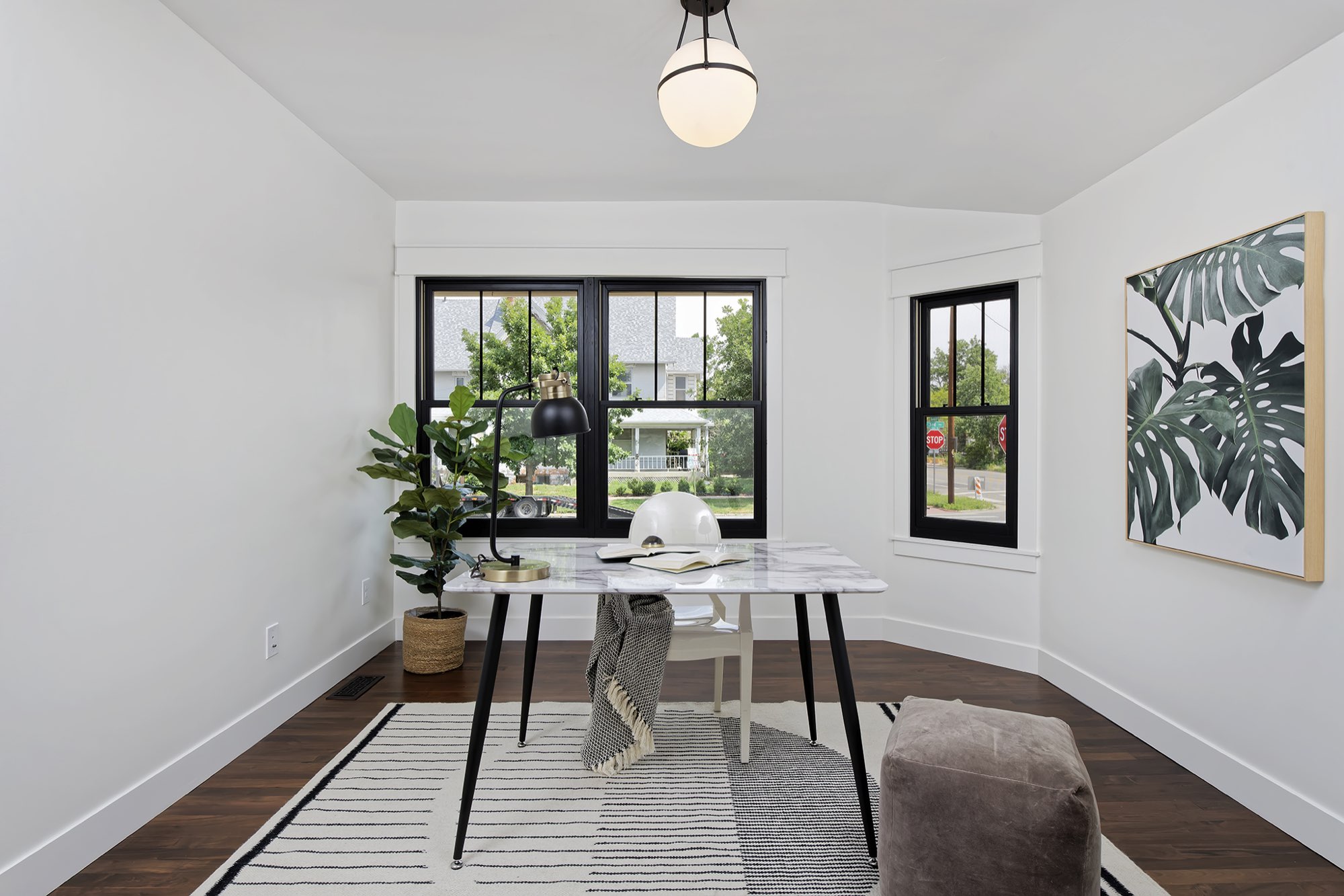 Front study with a bay of black-framed windows, white walls and dark wood floors