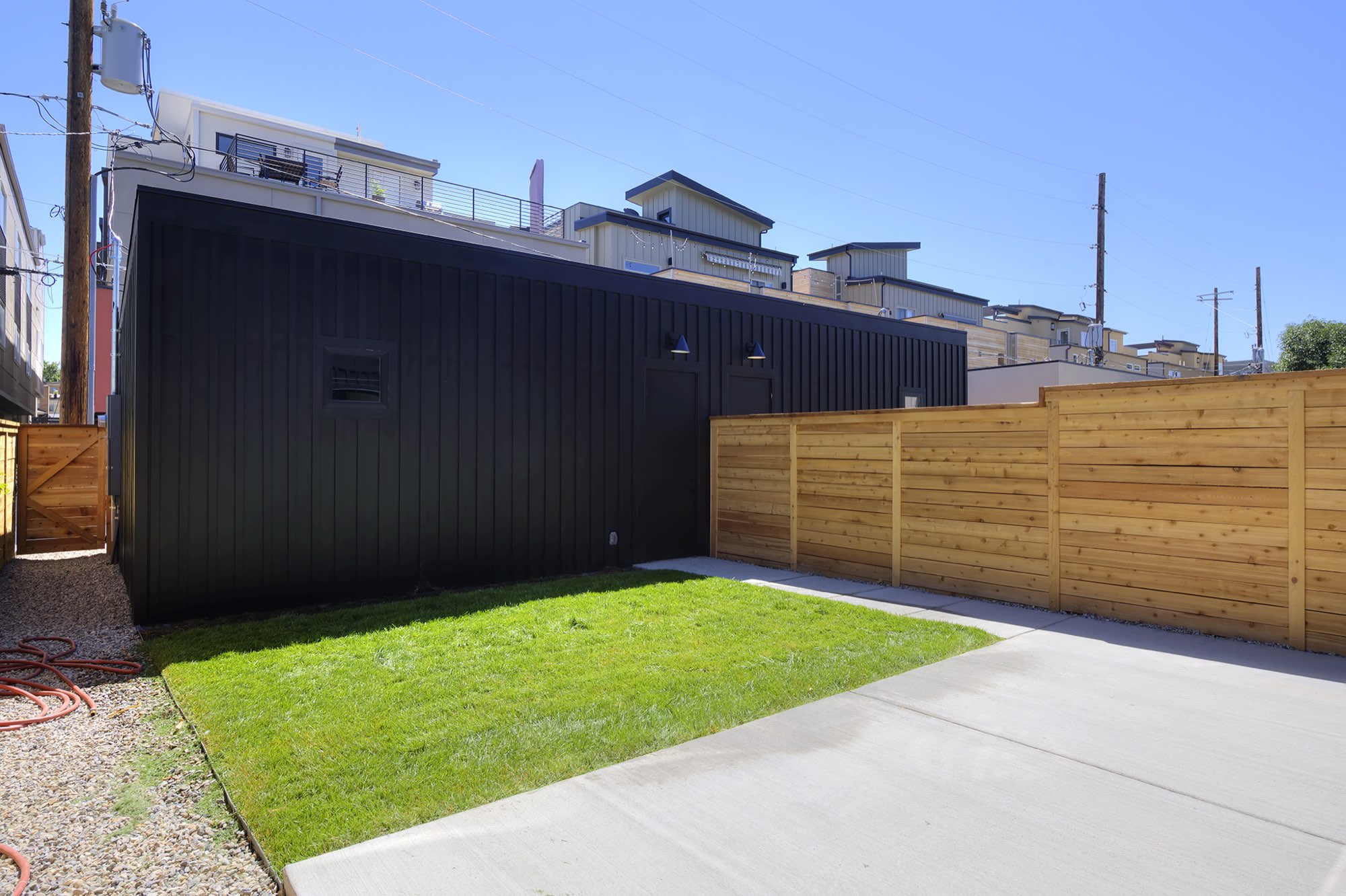Backyard lawn and concrete patio beside a wood fence and the black rear wall of the house