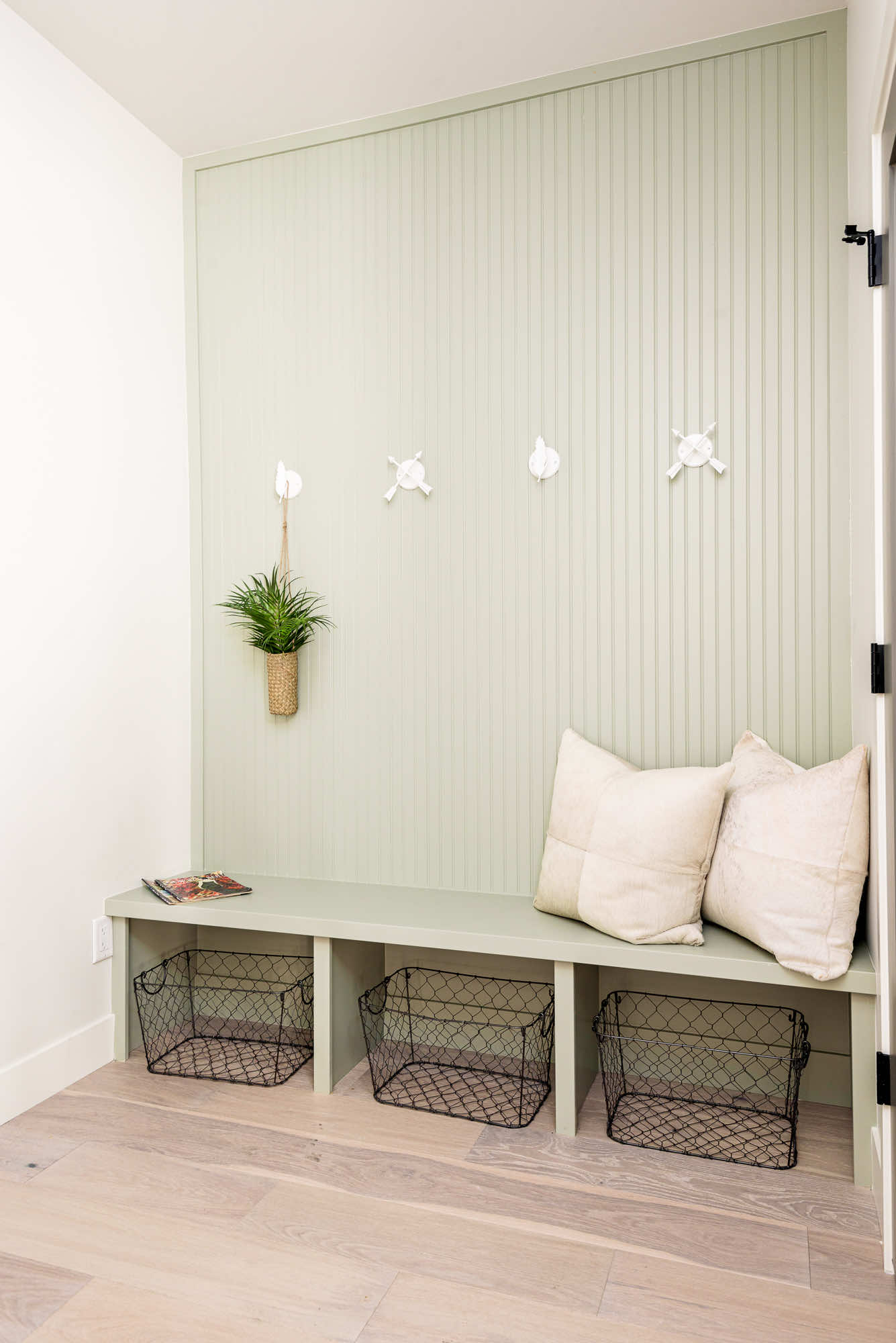 Mudroom bench with three cubbies and coat hooks on a pale green slat wall