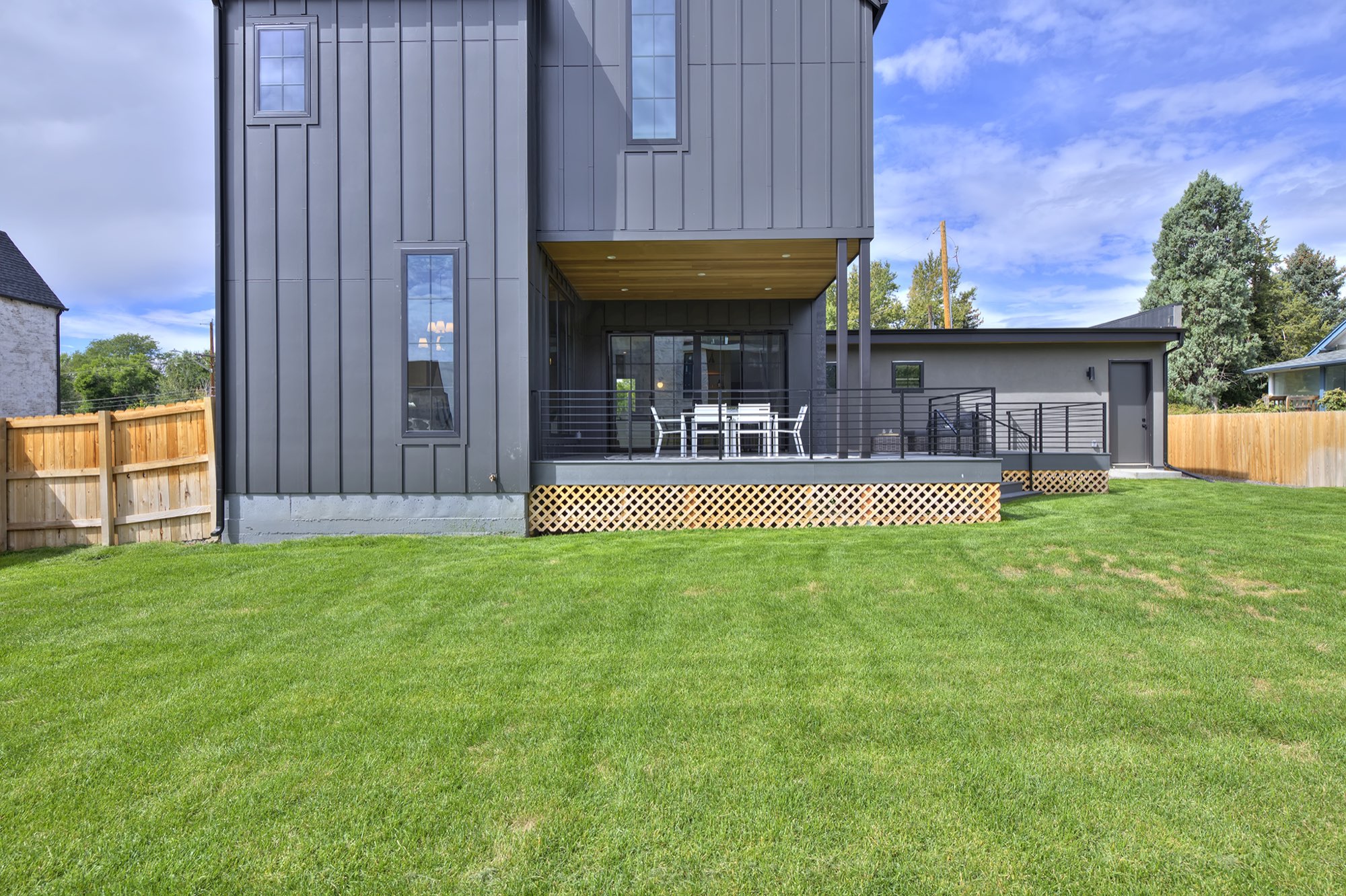 Back of the two-story house with a covered deck, black horizontal railing and a wood privacy fence
