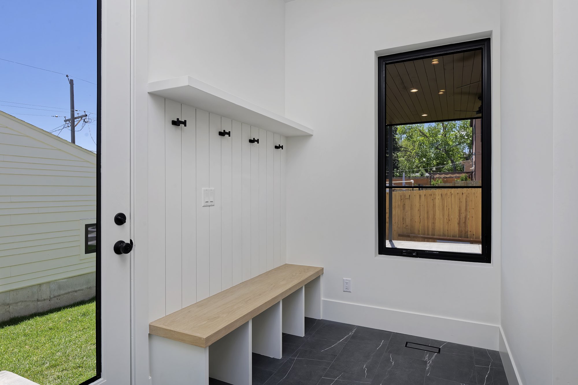 Mudroom with white vertical paneling, black coat hooks, a wood-top bench with cubbies and dark tile floor