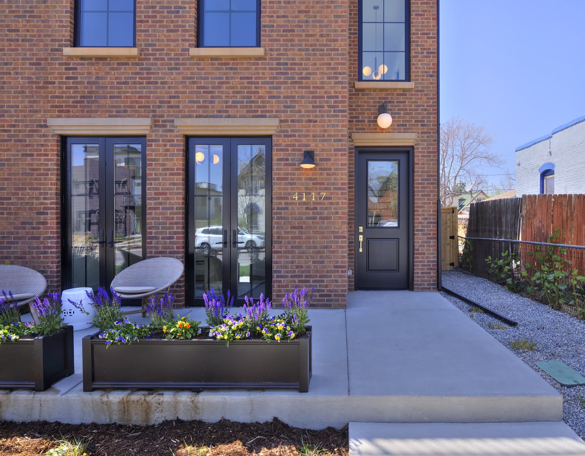 Front of the Denver custom home in red brick with black-framed French doors, a black front door, planter boxes with purple flowers and a concrete walk