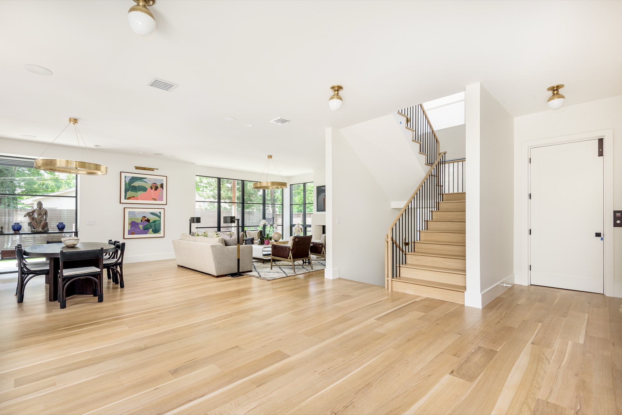 Open main level with light wood floors, a staircase with a black railing and black-framed windows
