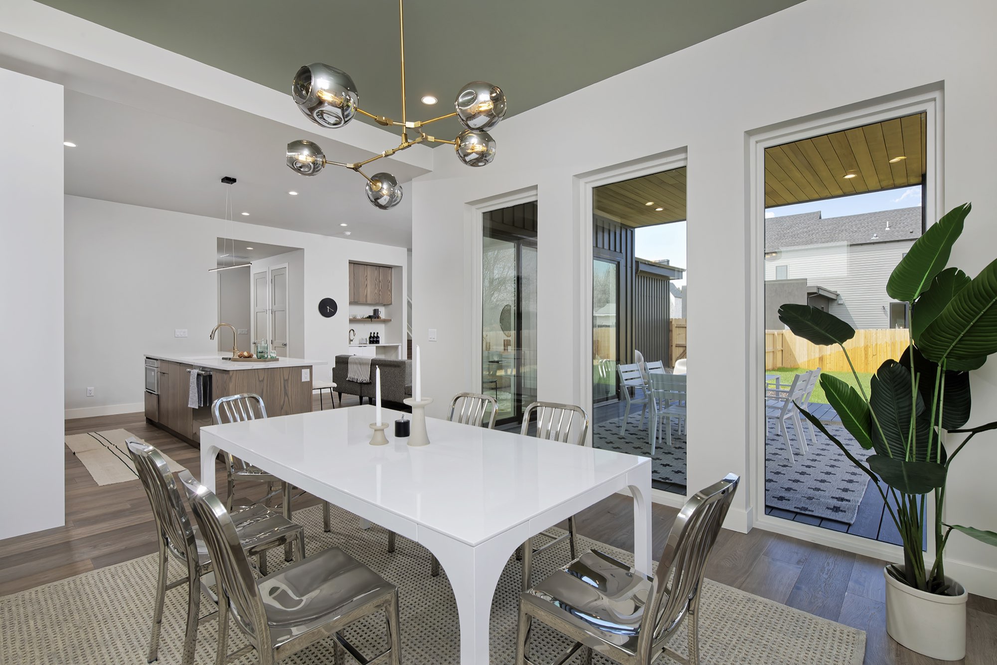 Dining room with a sage green ceiling, a white table with metal chairs, a brass chandelier and a long window