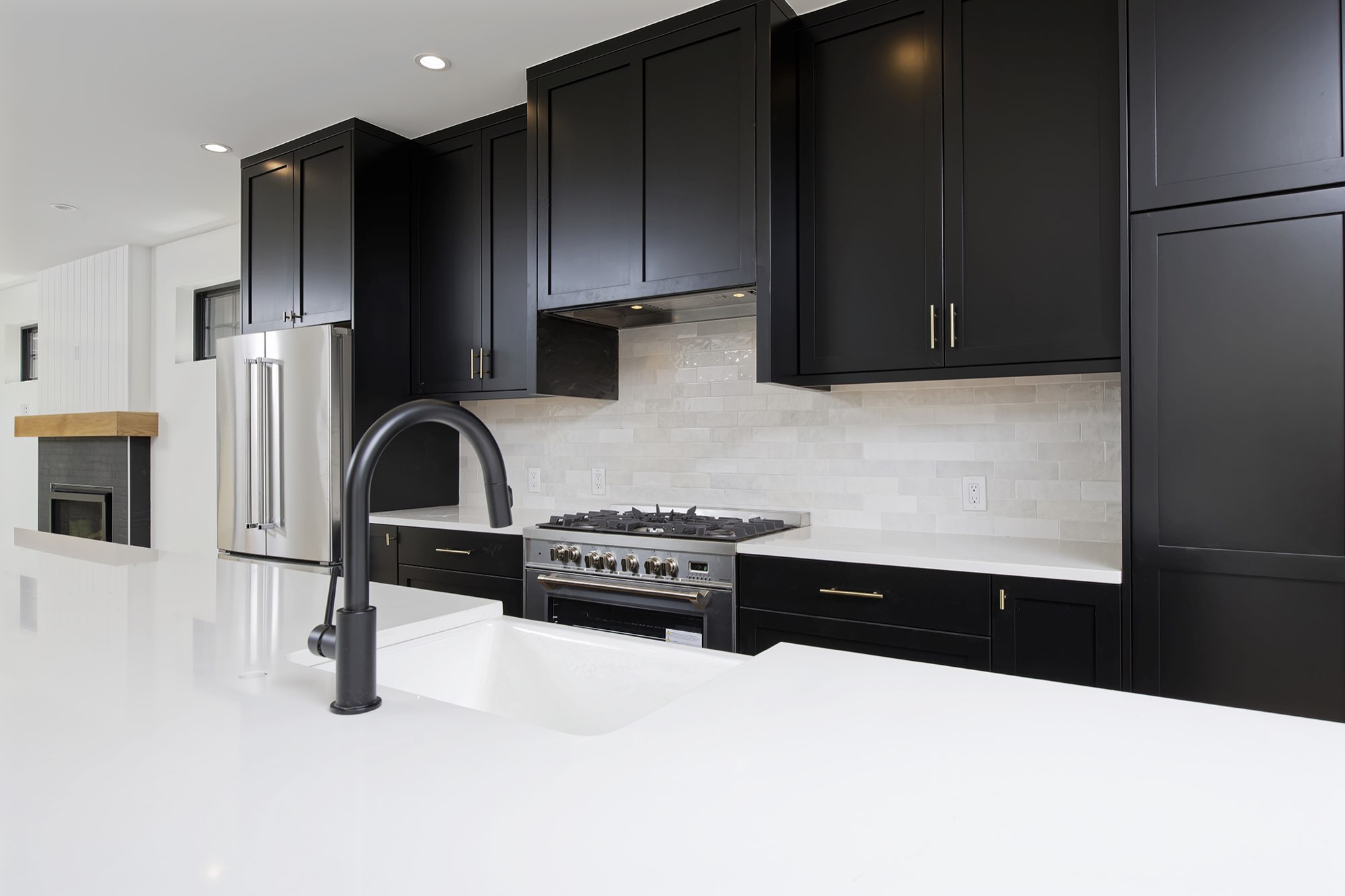 Black faucet at the white island sink, with a stainless range and soft tile backsplash behind
