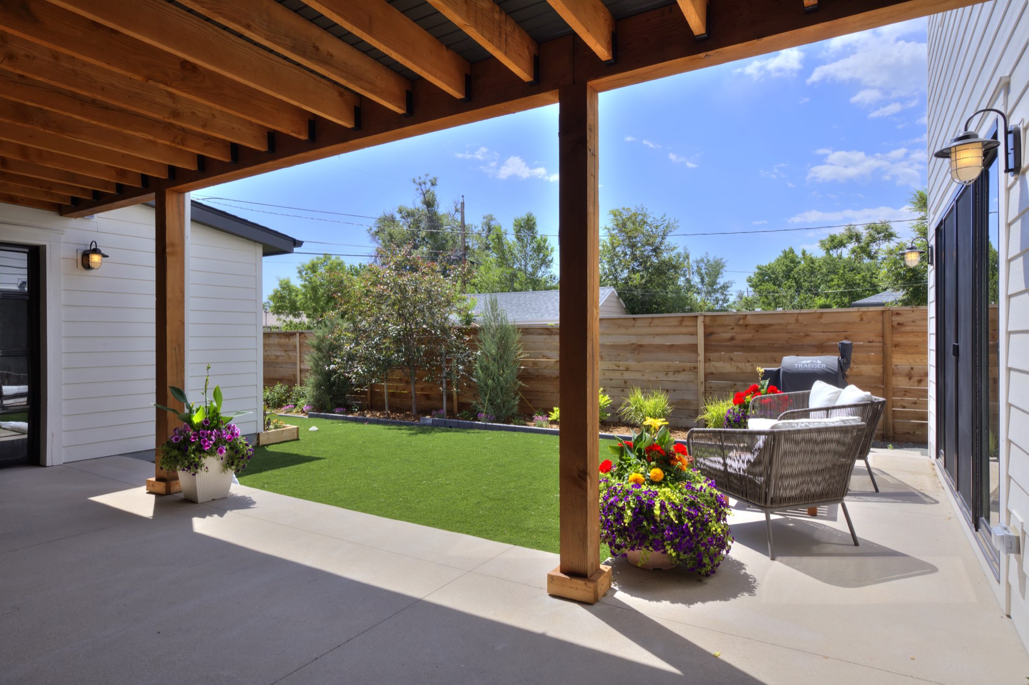 Covered patio looking out to the lawn and wood fence with a seating area and flower pot