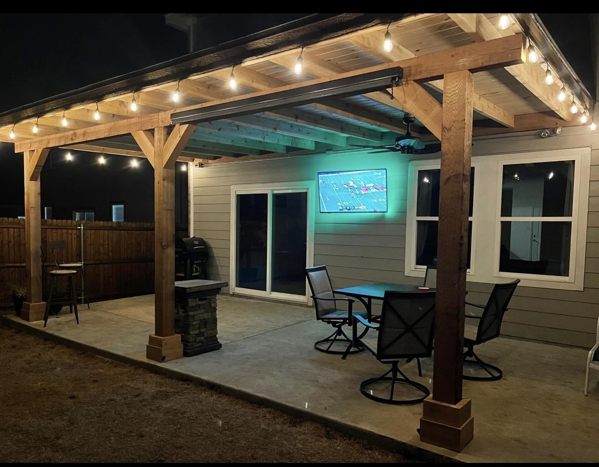 Covered patio with cedar beams, string lighting and a stone-base column, lit at night, in Texarkana, TX
