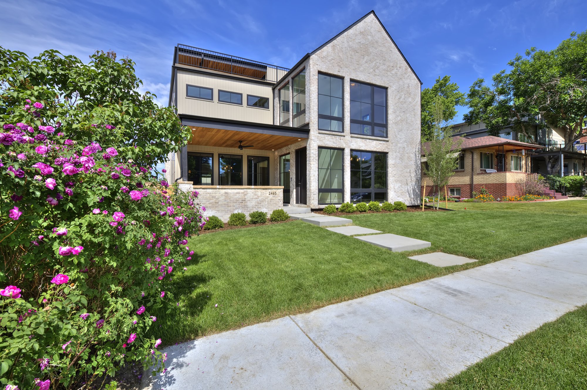 Front of the new custom home in Denver with a tall pale brick gable, black-framed windows, a covered porch and a lawn with stepping stones