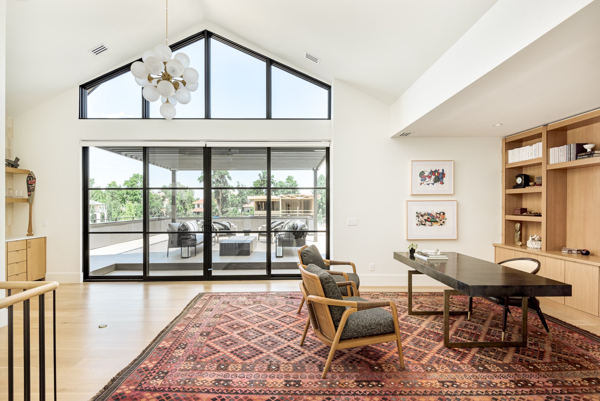 Vaulted study with a gabled window, a red patterned rug, a dark desk and glass doors to the terrace
