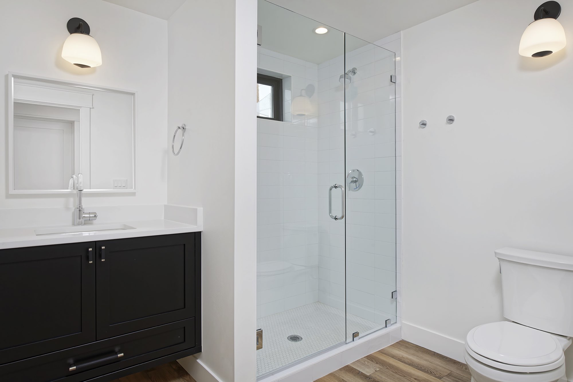 Bathroom with a black vanity, white quartz top and a frameless glass shower