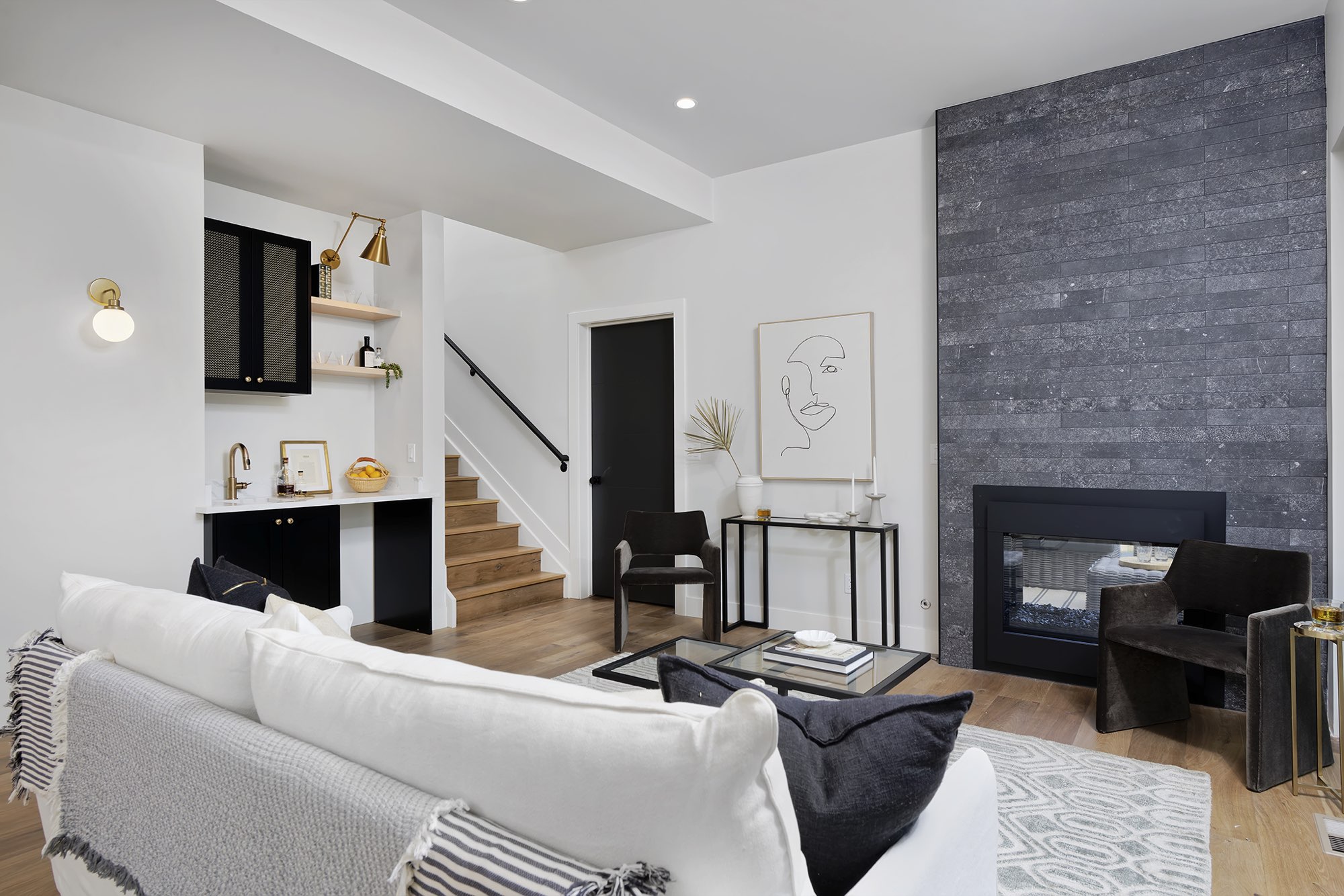 Living room with a see-through fireplace in dark stone, a black interior door and a wet bar with stairs beyond