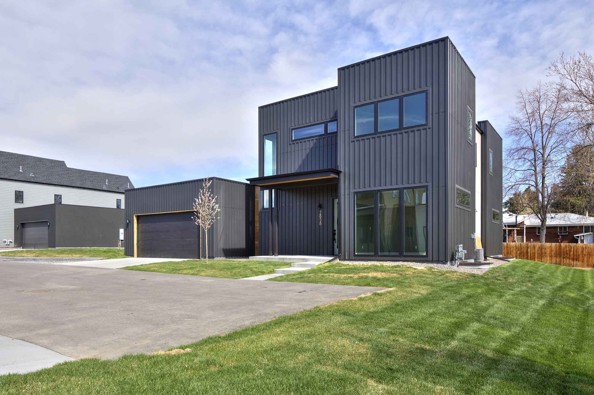 Angled view of the charcoal two-story home with tall black-framed windows, a wood canopy over the entry and a new lawn