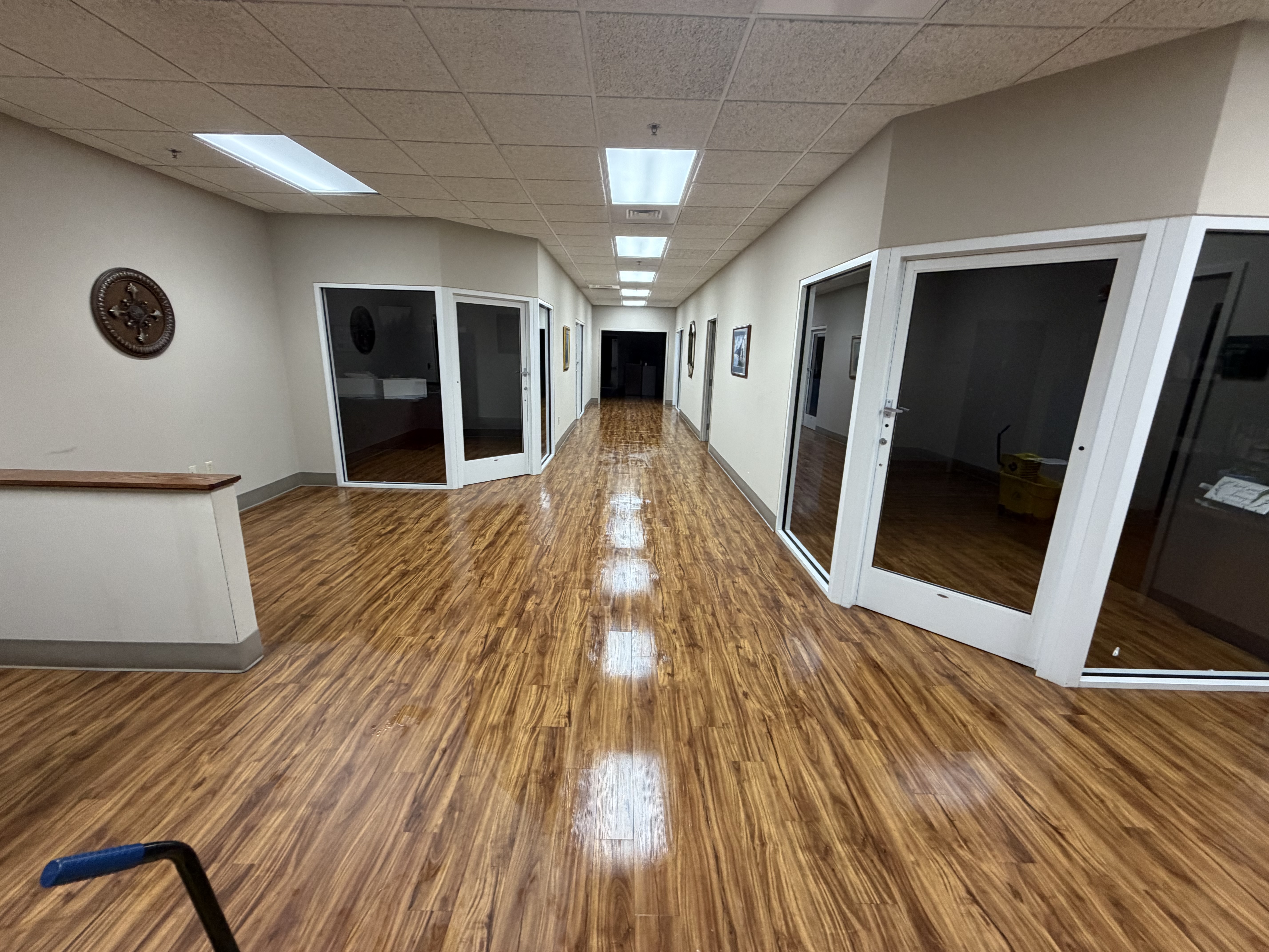 Long office corridor with glass office fronts and a high-gloss wood-look floor
