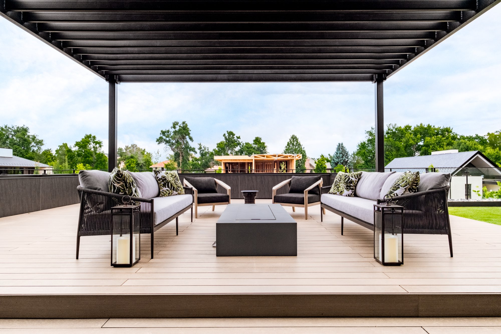 Upper deck with sofas around a fire table under a black pergola, with a view over trees and neighboring roofs