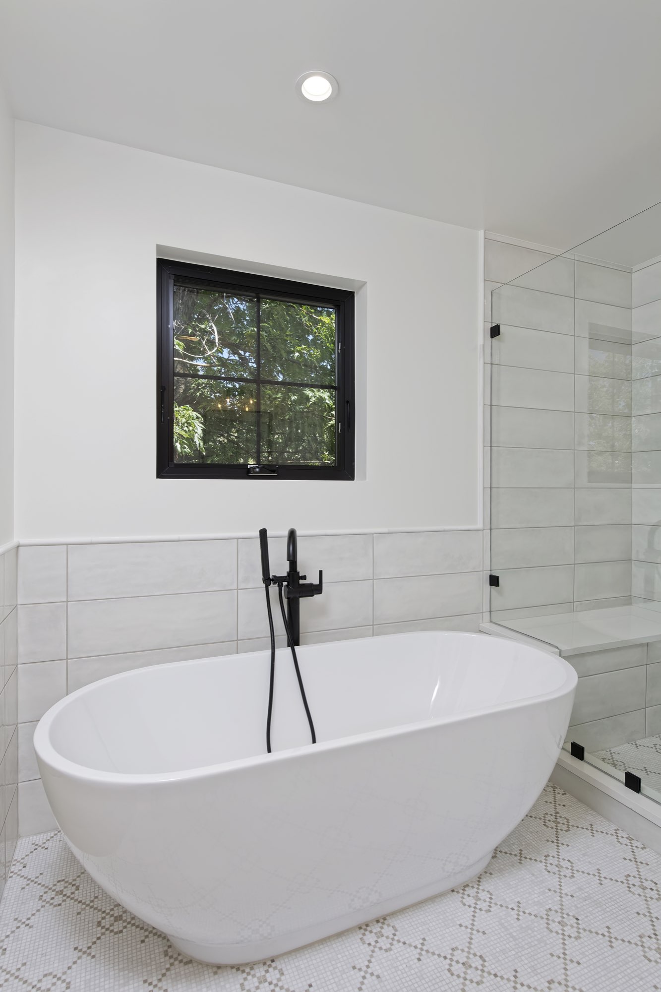 Freestanding white tub with a black floor-mounted faucet under a black-framed window beside a glass shower