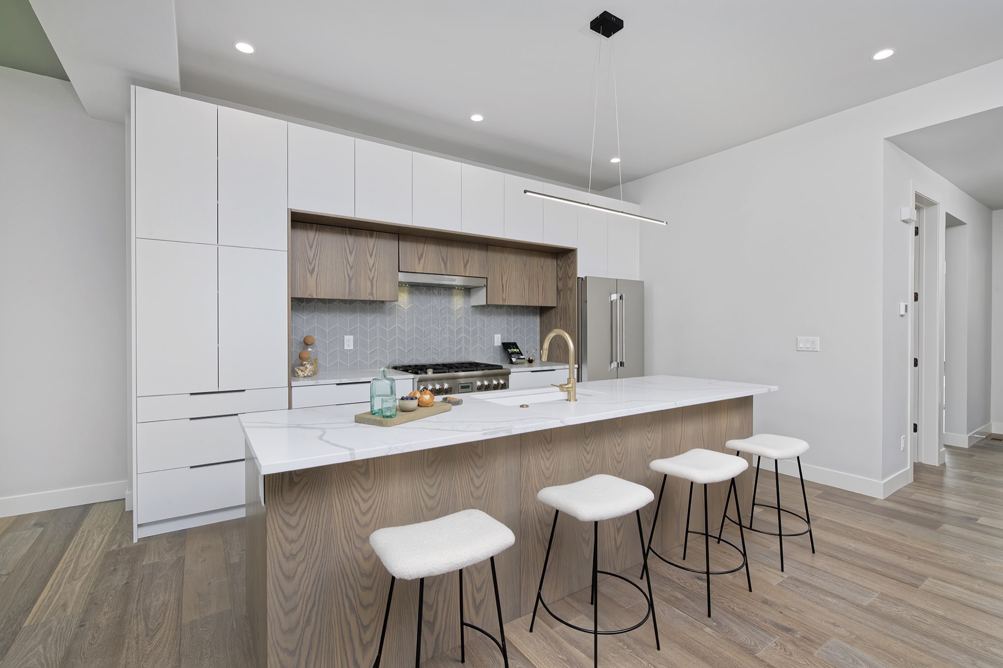 Kitchen from the end of the island with white cabinets, a wood-toned hood inset and a long pendant light