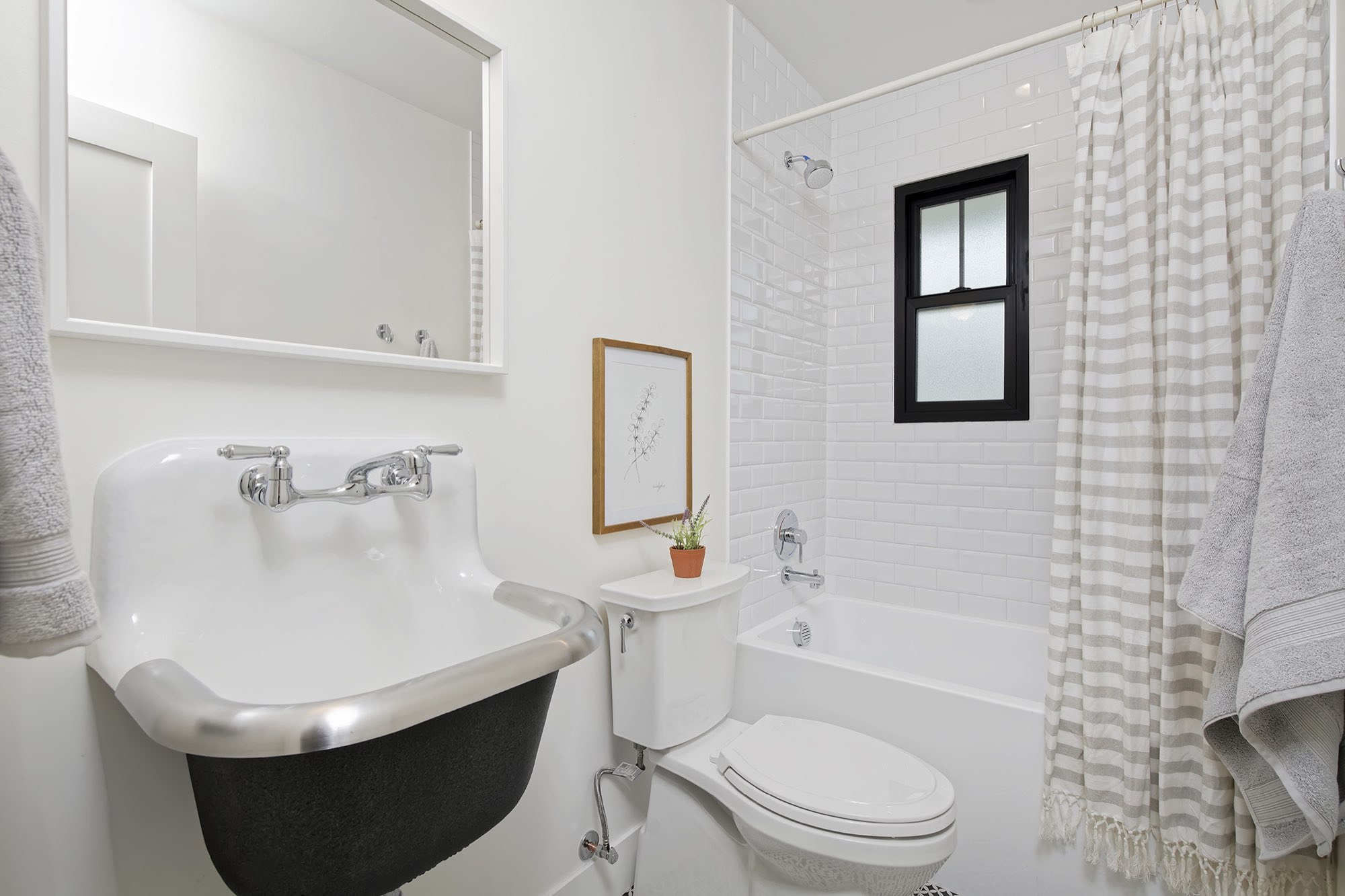 Bathroom with a wall-hung sink, white subway tile tub surround and a black-framed window
