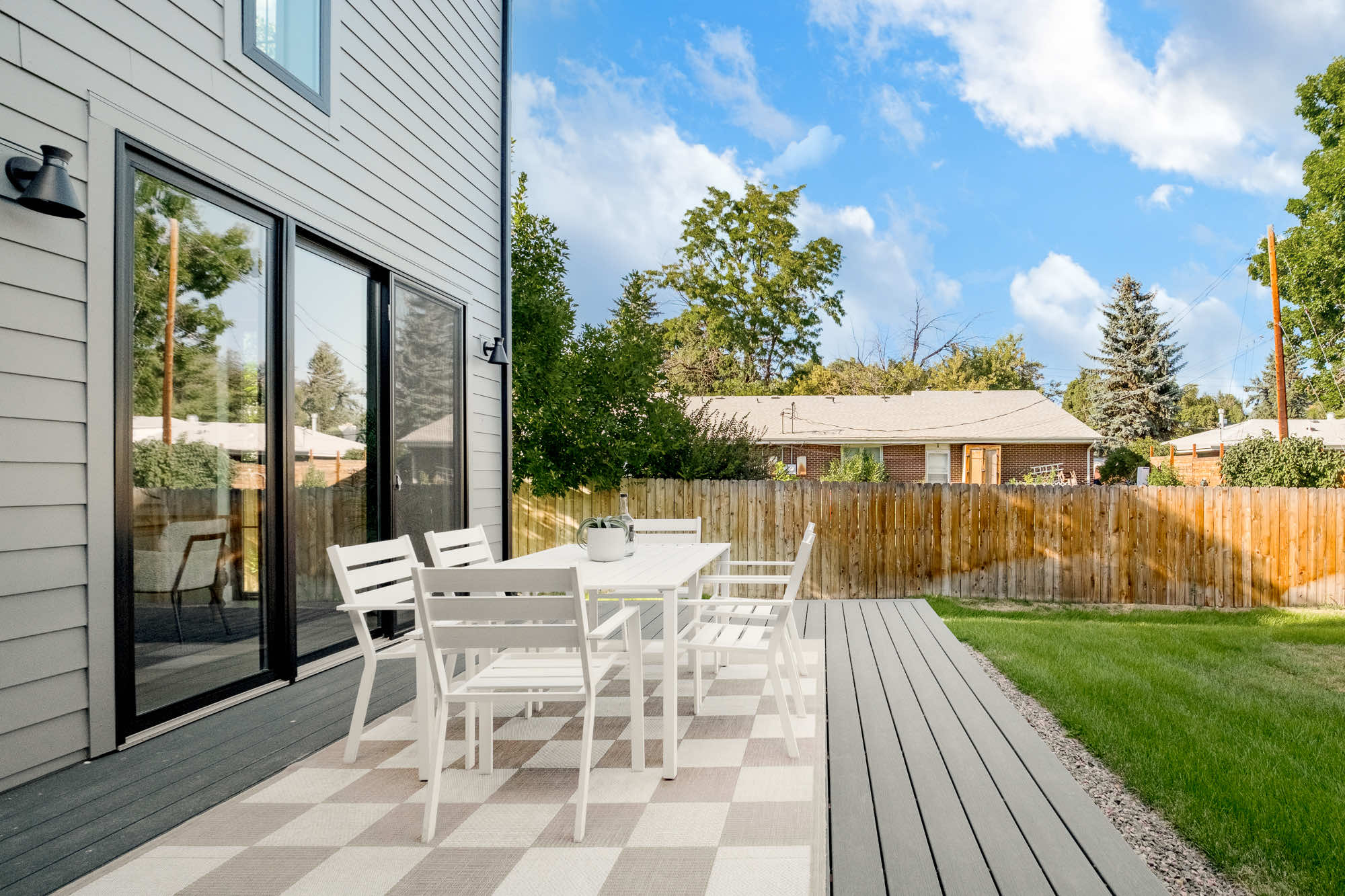 Back deck with a white dining table and a black slider, with the fenced lawn beyond