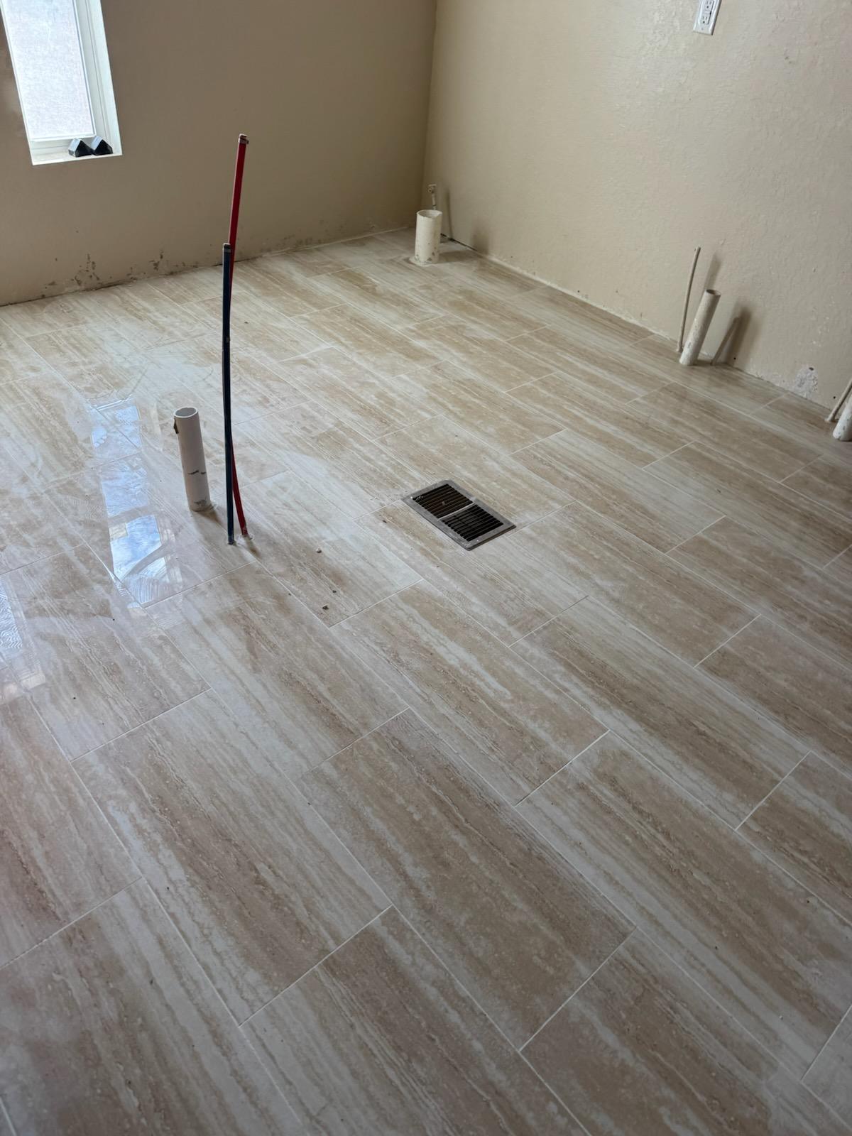 Travertine look vinyl tile part way through installation in a mobile home room with pipe stub-outs and a floor vent
