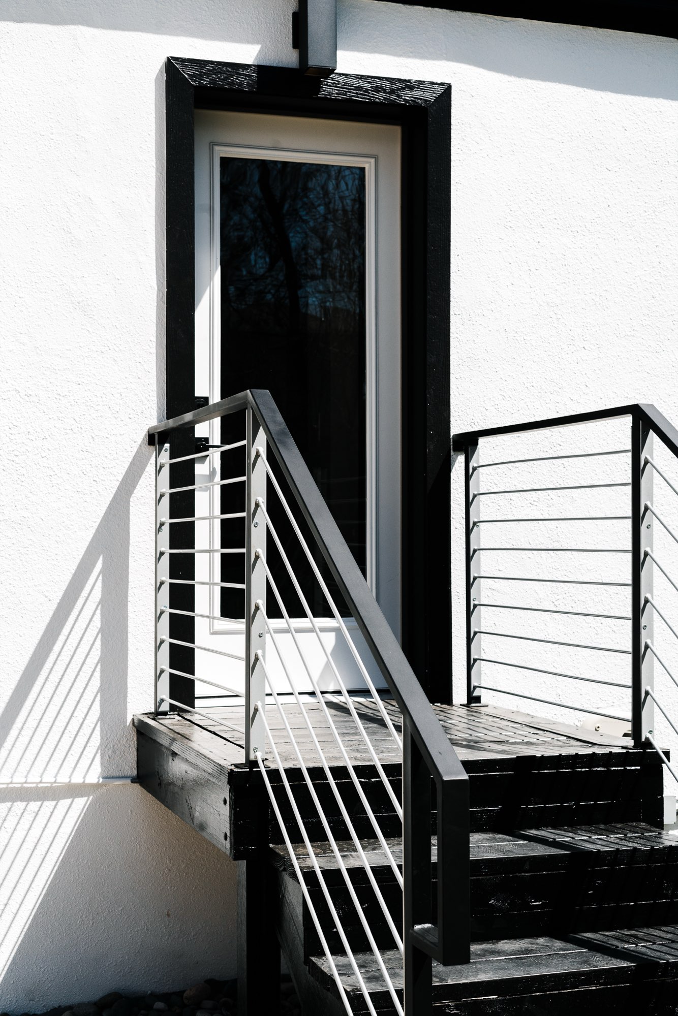 Close view of the black back stair and railing beside the white wall and black trim