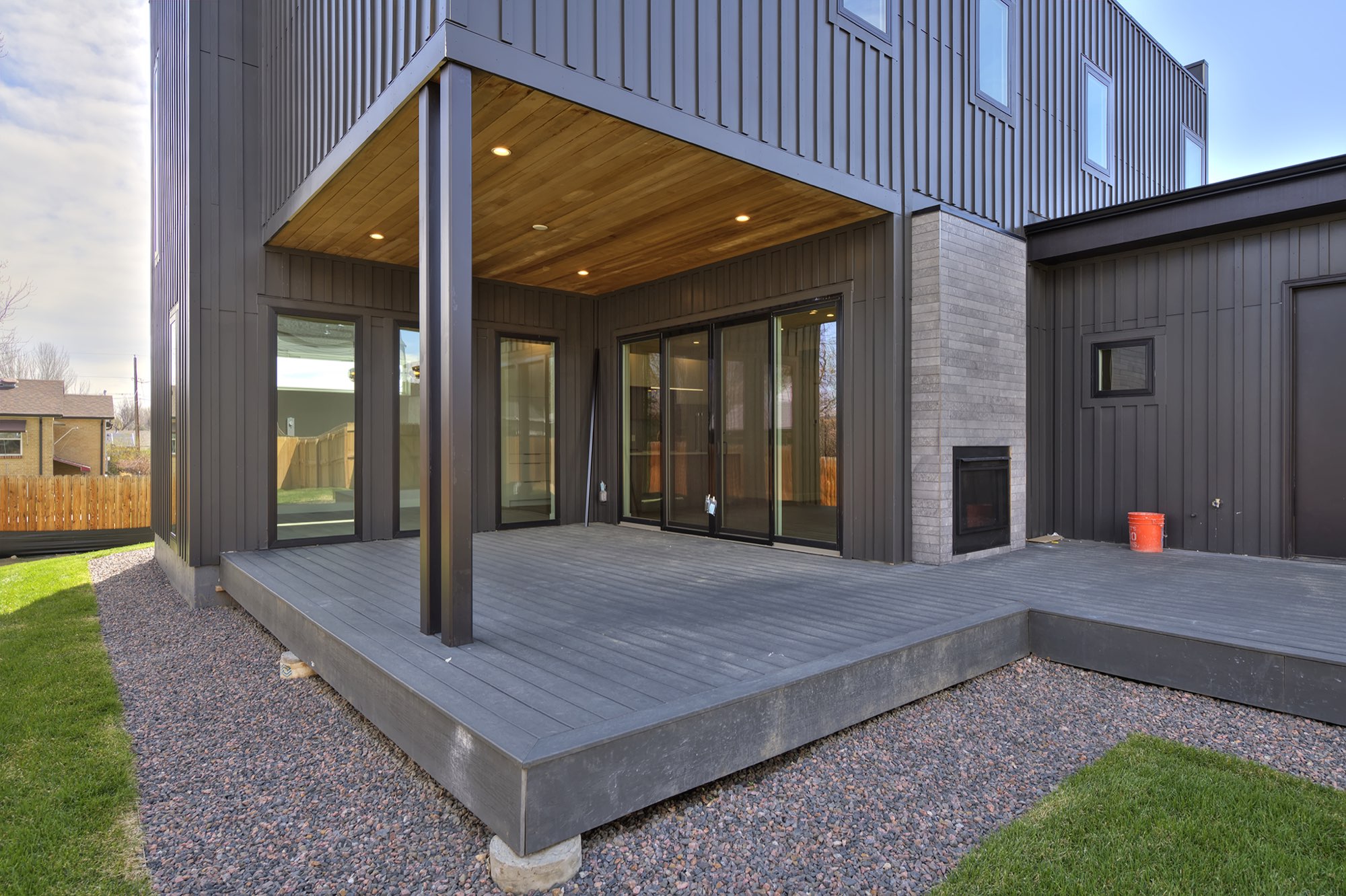 Deck corner with a gray fireplace wall, black-framed sliders and a gravel edge
