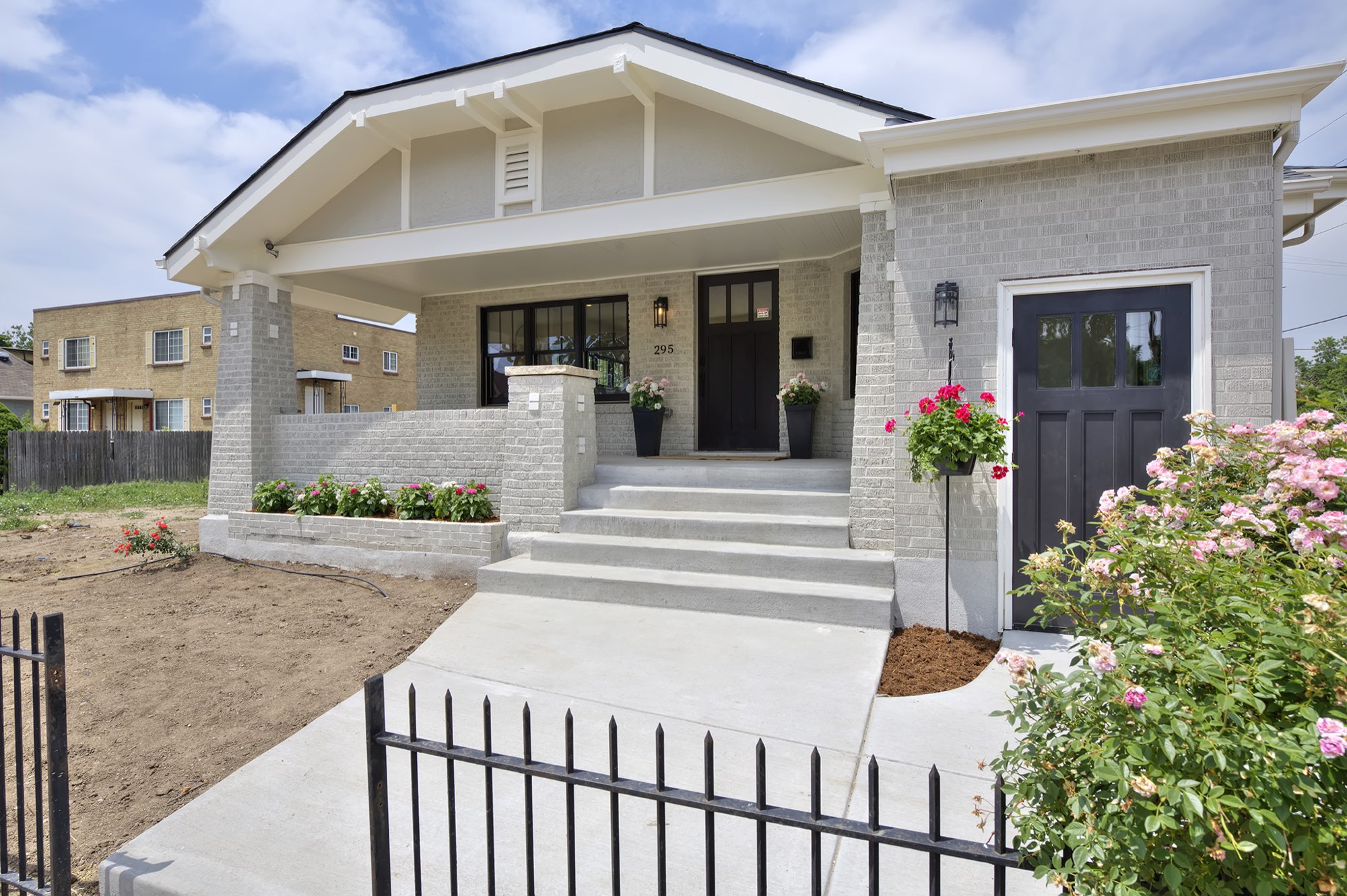 Front of the renovated 1893 landmark bungalow in Denver with pale gray brick, a deep covered porch, black-framed windows and a black side door