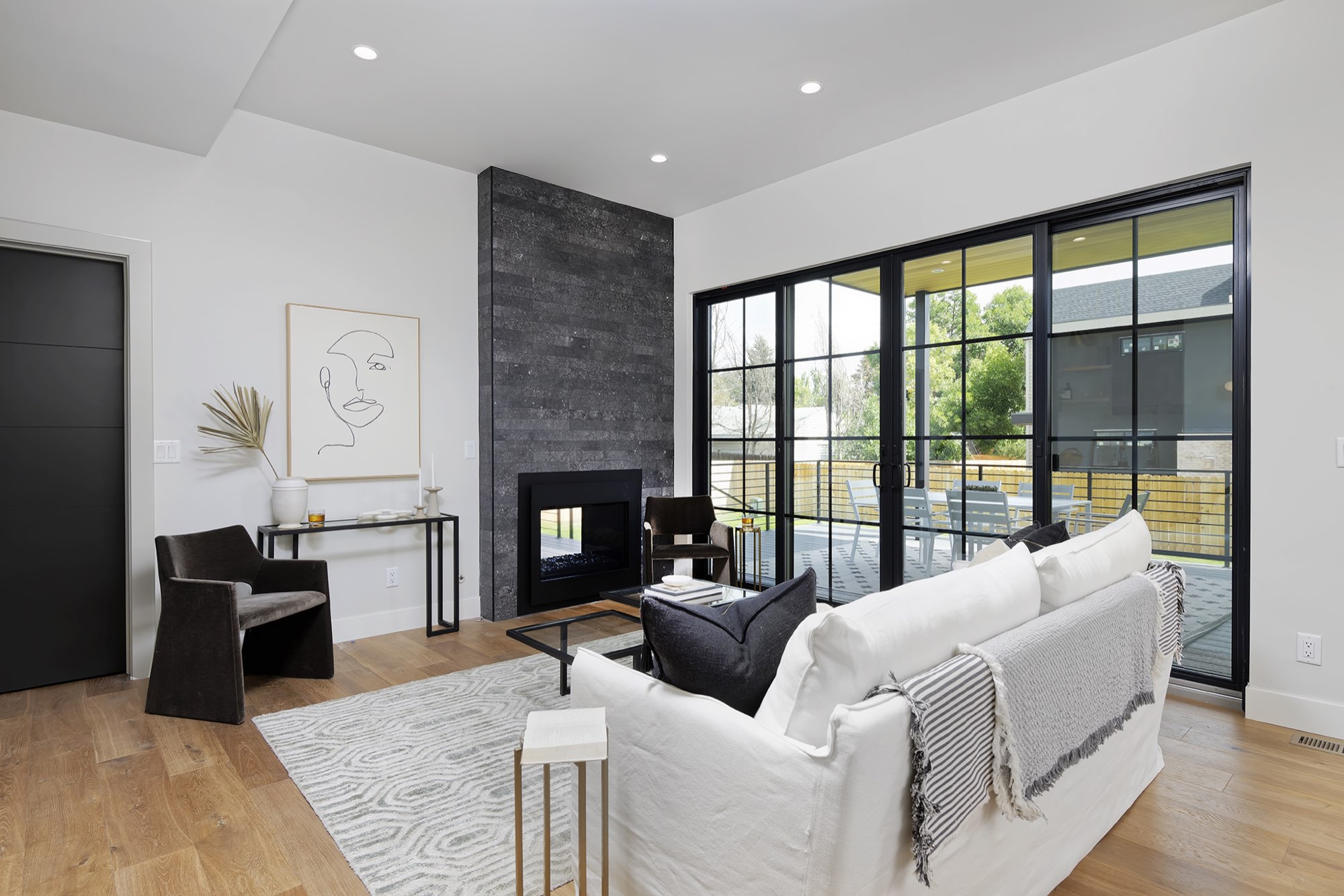 Living room with a dark stacked-stone fireplace wall, black-framed sliding doors to the deck and wood floors