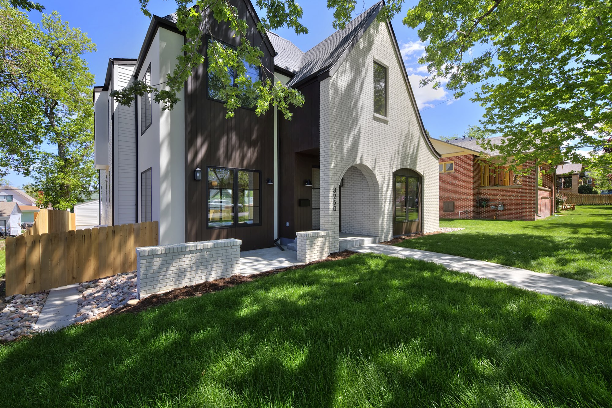 Angled front of the Tudor-style home with white brick gable, dark vertical siding, arched entry and a low brick wall