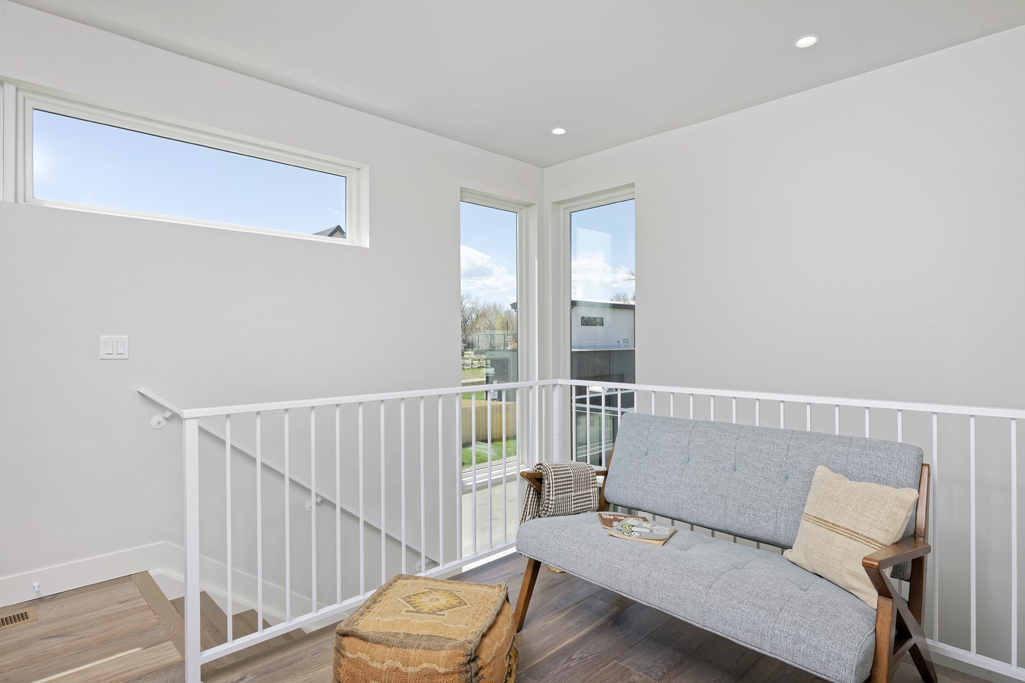 Upstairs landing with a white railing, a long window and a seating spot at the top of the stair