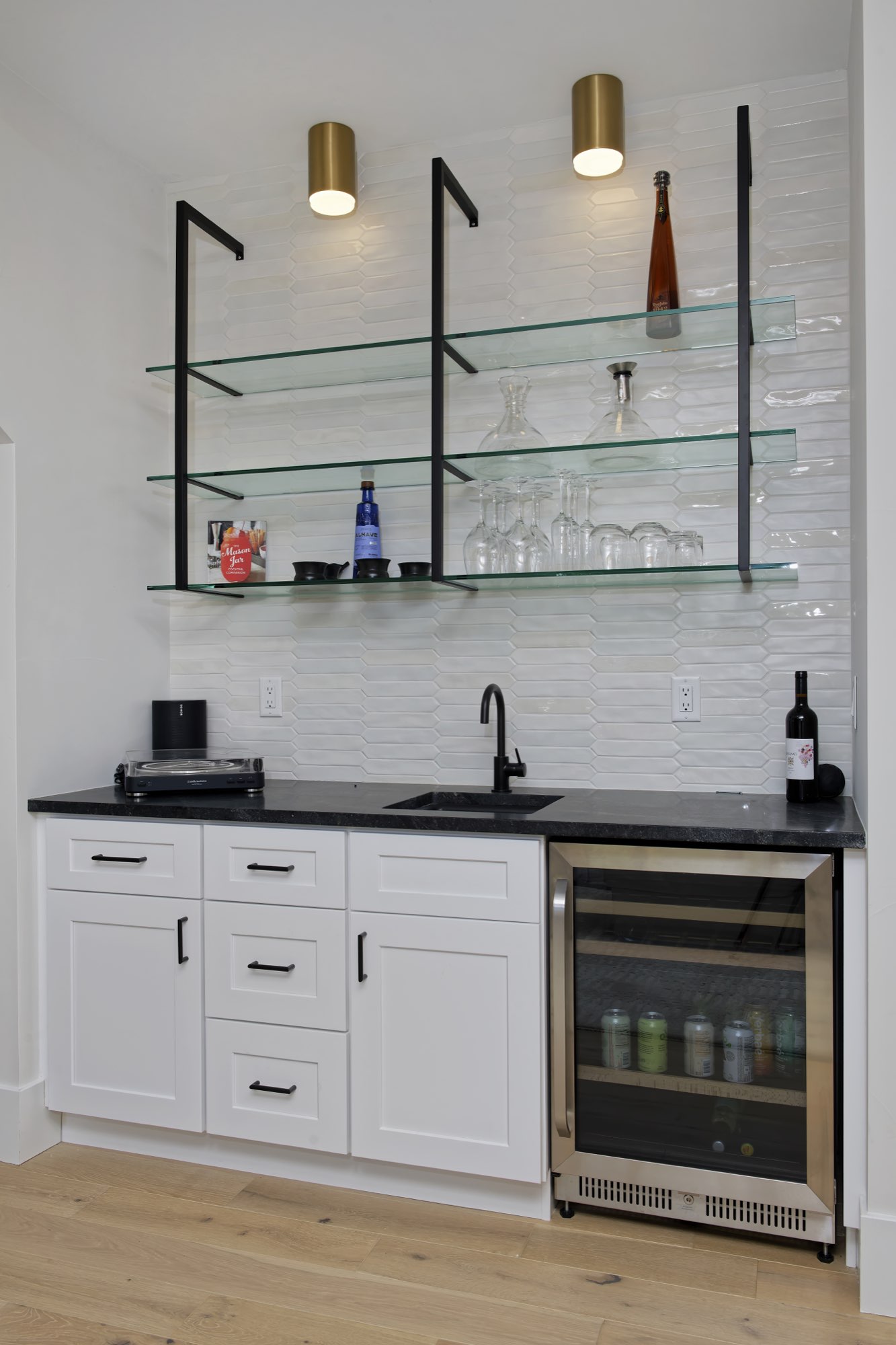 Wet bar with white cabinets, black counters, a beverage fridge and glass shelves on black brackets