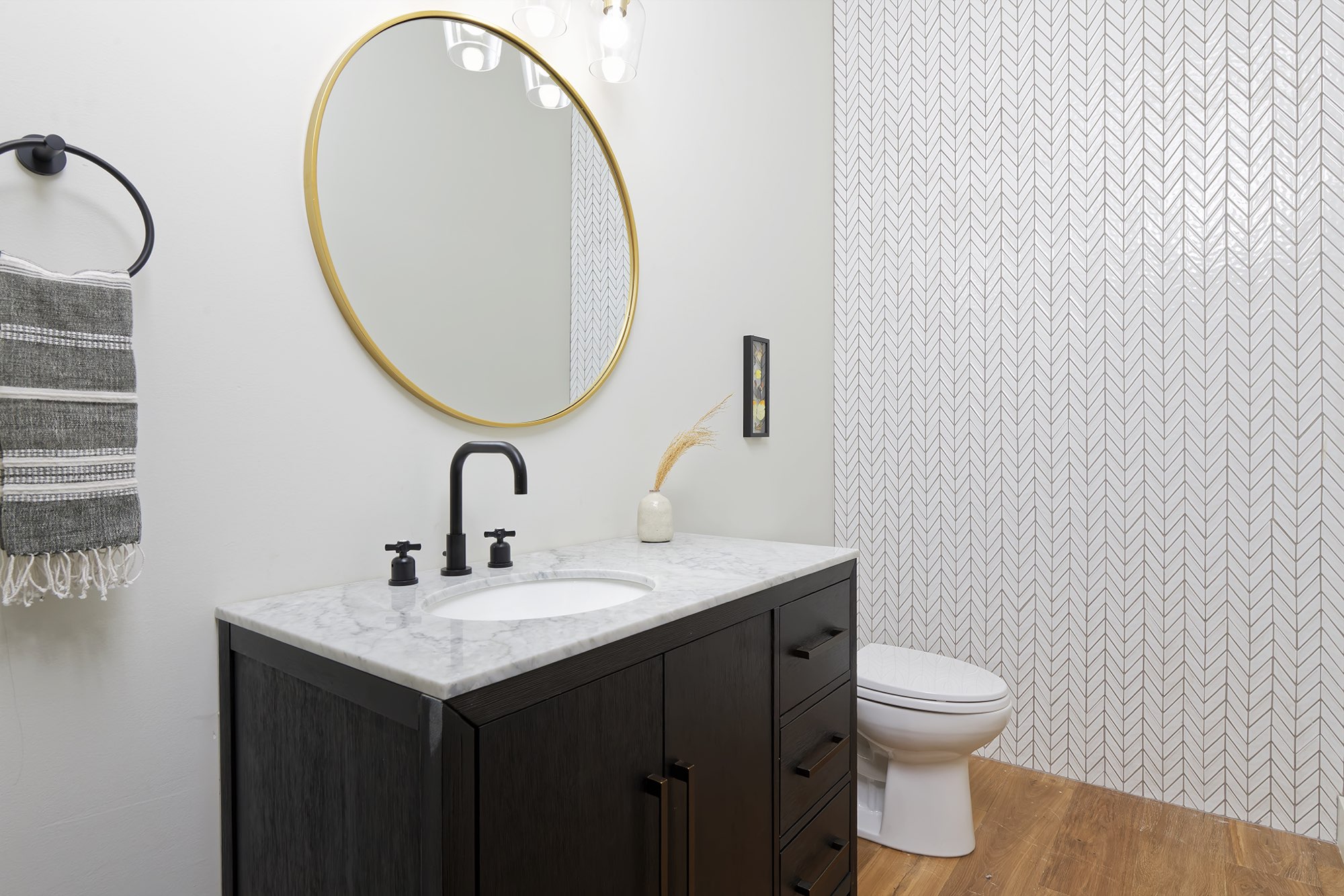 Powder room with a round brass mirror, a black faucet and a white chevron tile wall