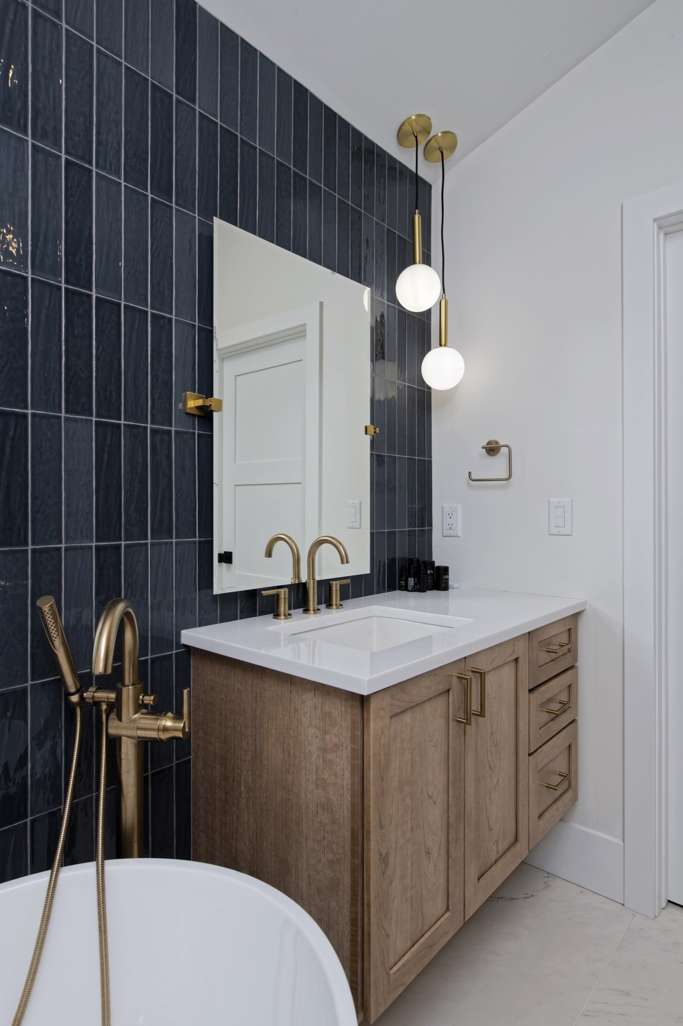 Wood vanity with a white top and brass fixtures against navy tile with a globe light pendant