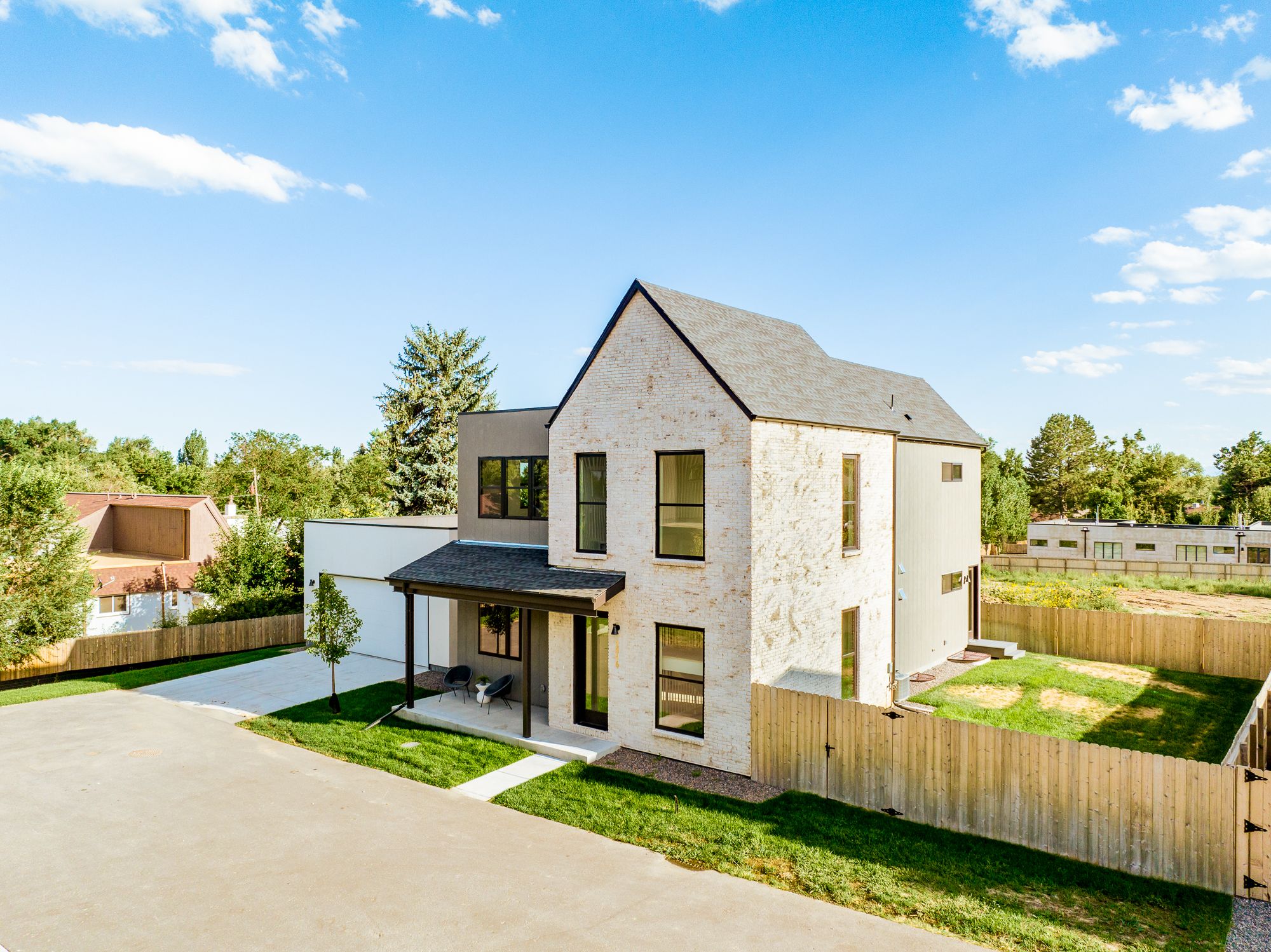 Angled front of the new custom home in Wheat Ridge with a whitewashed brick gable, gray siding, dark shingle roof and fenced side yard