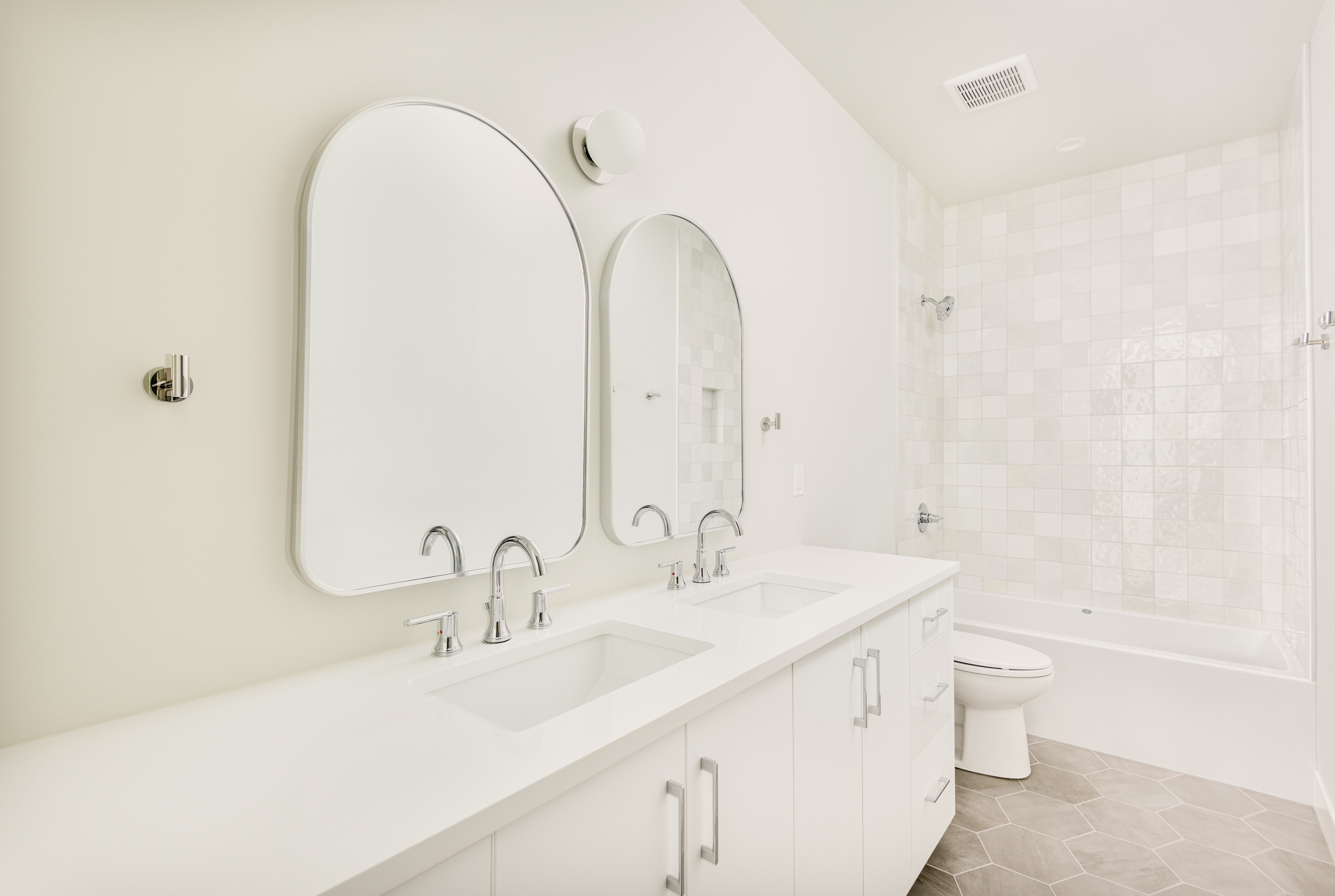 Hall bathroom with arched mirrors over a white double vanity